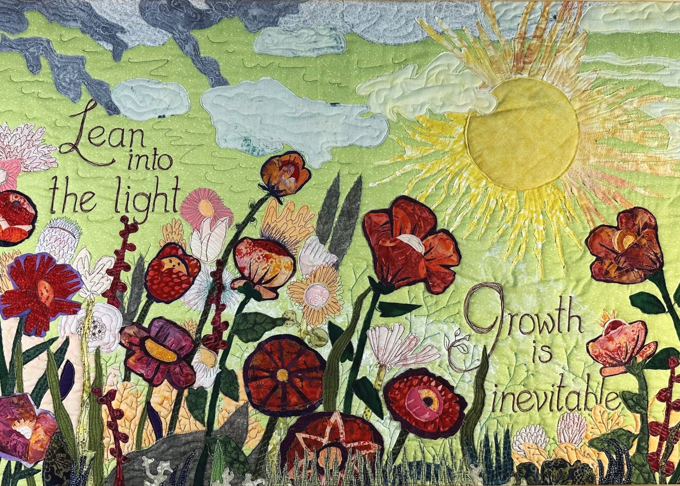Colorful quilt with sun, clouds, flowers, and moths. Text reads 'Lean into the light'.