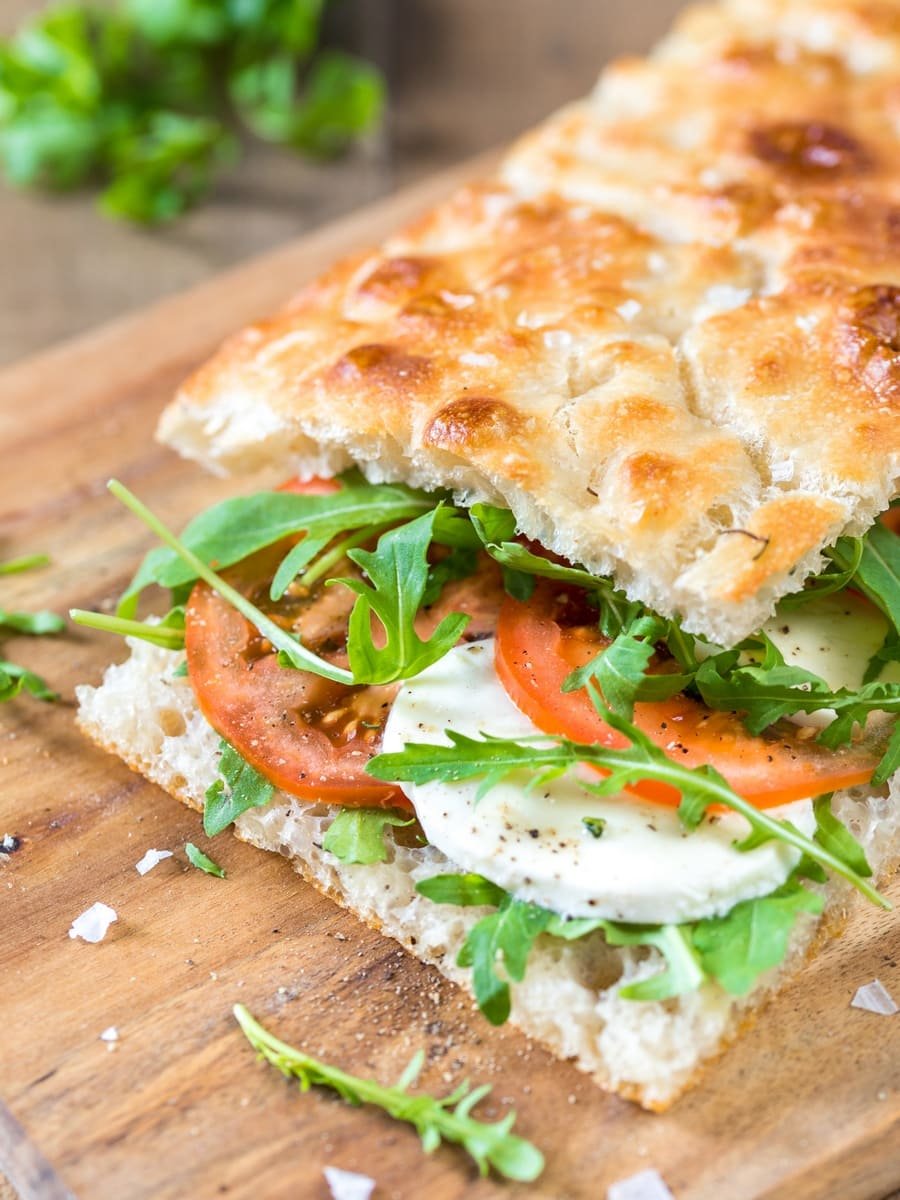 Close-up van een sandwich met tomaat, rucola, een gepocheerd ei en kaas op een houten snijplank.