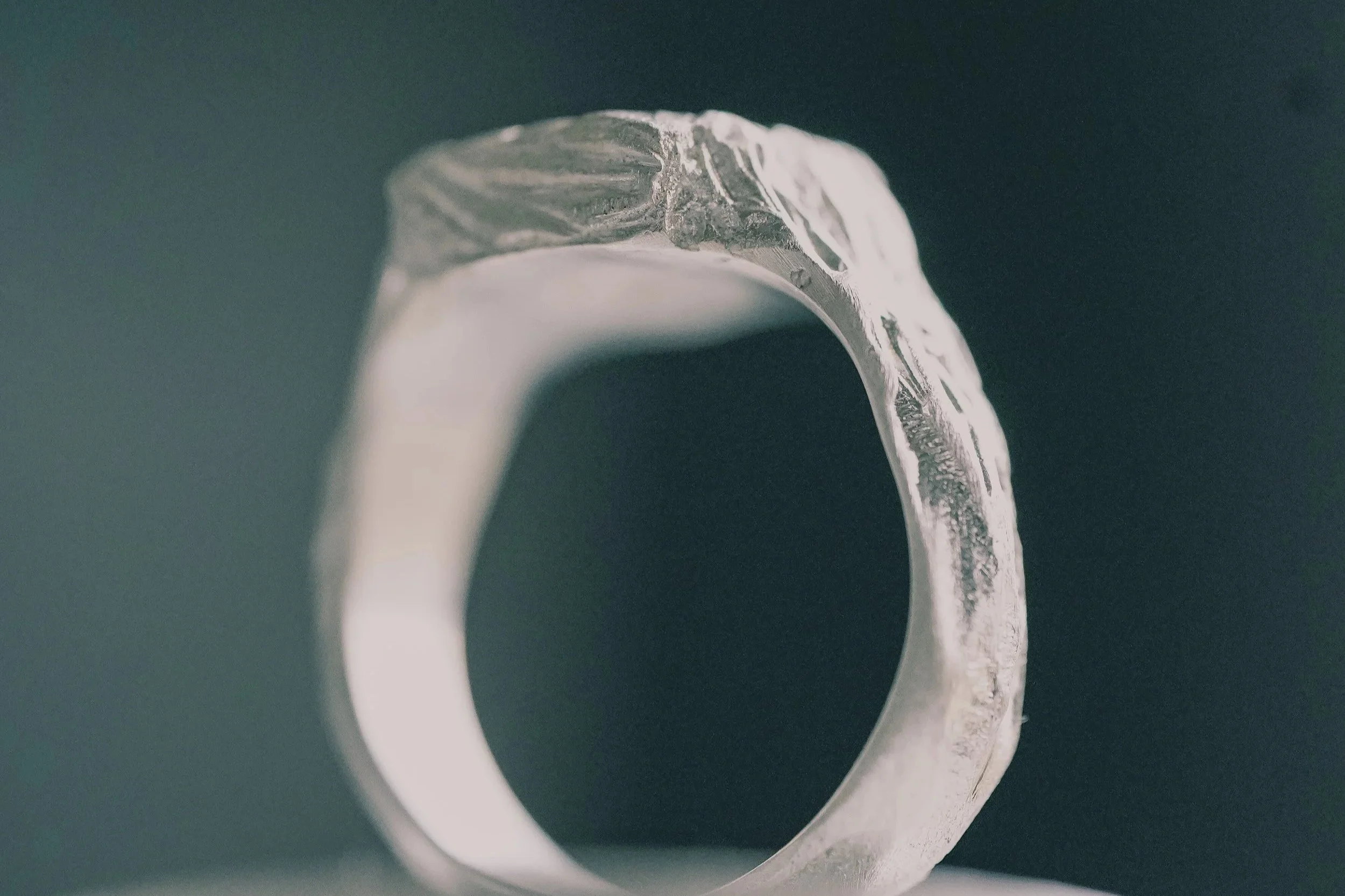 Close-up of a silver ring with a textured surface on a dark background.