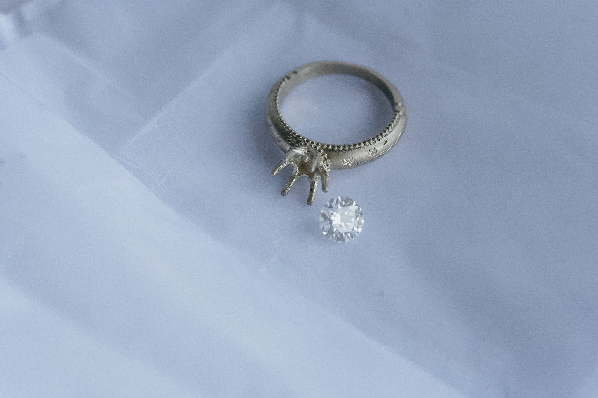 A silver ring with intricate engravings and beaded details, a dangling star-shaped charm, and a large round-cut diamond gemstone are placed on a white surface.