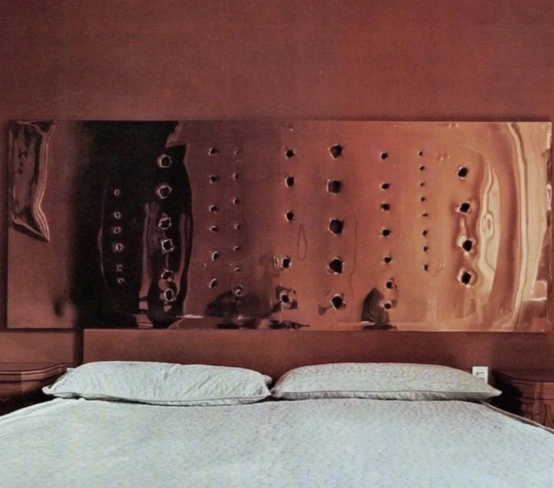 A bed with white bedding and two pillows in front of a decorative wooden wall with holes and patterns.