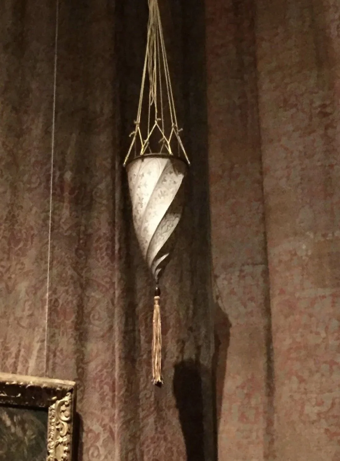 Ornate hanging lamp with a spiral design in a dimly lit room with textured wallpaper.