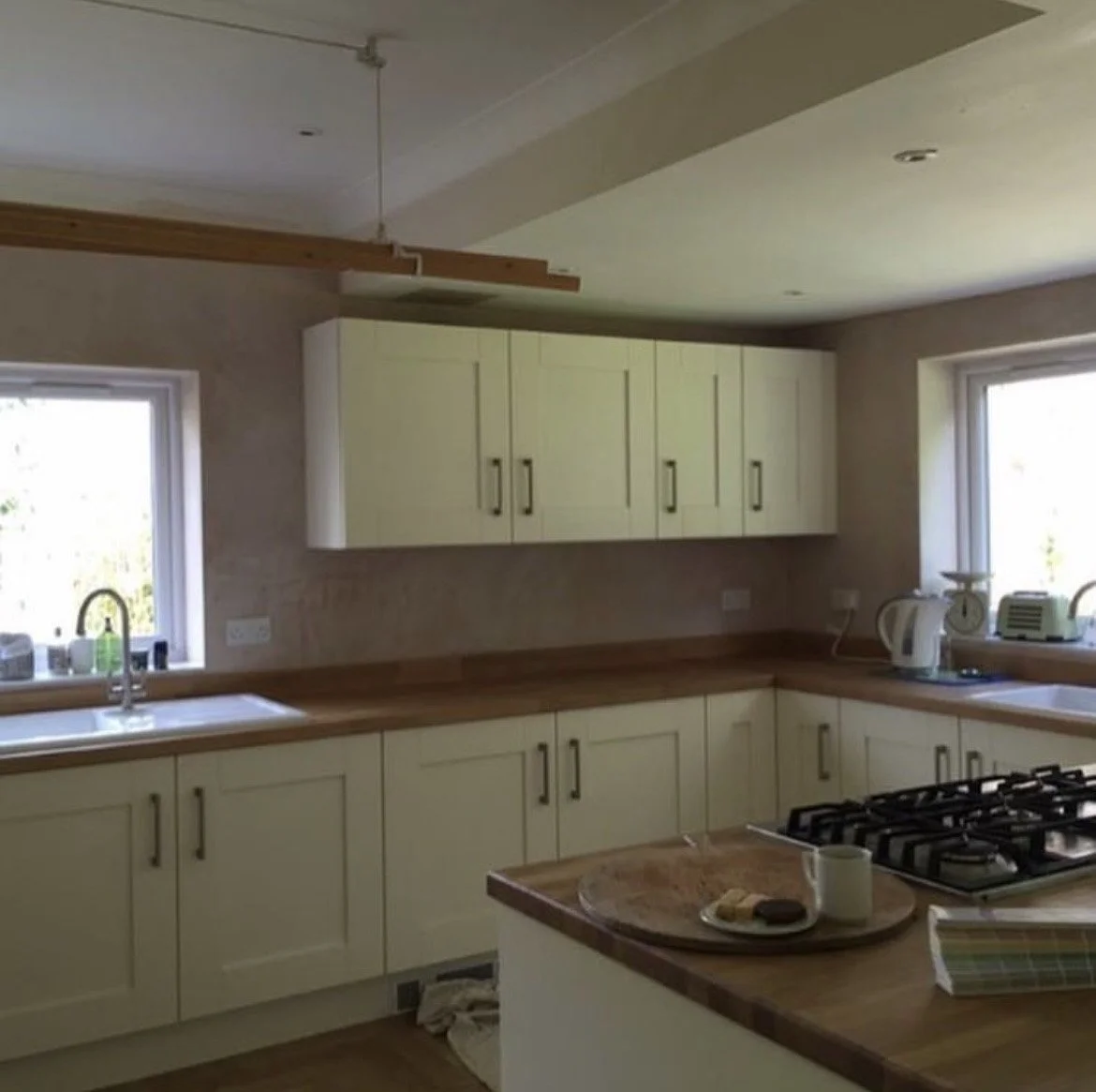 Modern kitchen with cream cabinets, wooden countertops, and two windows, featuring a stovetop island and small appliances.