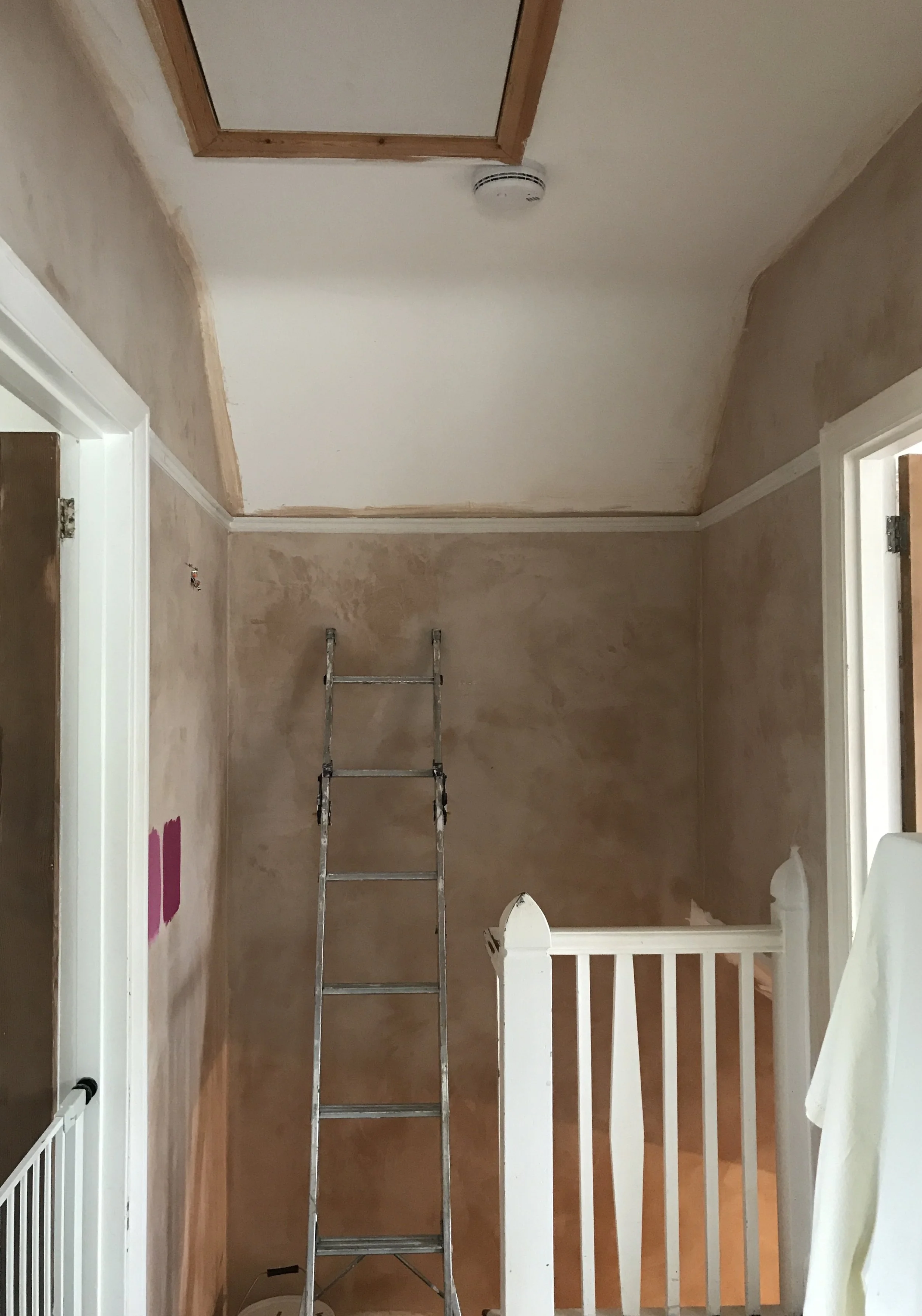 Interior room undergoing renovation with partially painted walls, a ladder, and an attic access door in the ceiling.