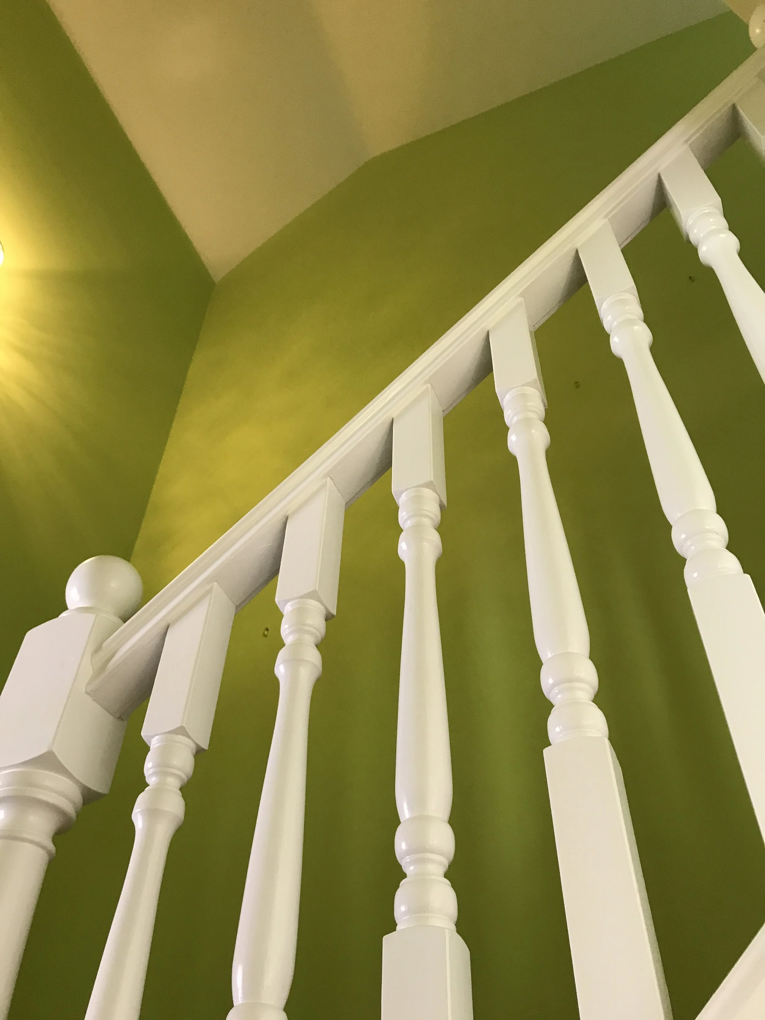 Looking up at a white wooden stair railing with turned balusters against a green wall and ceiling
