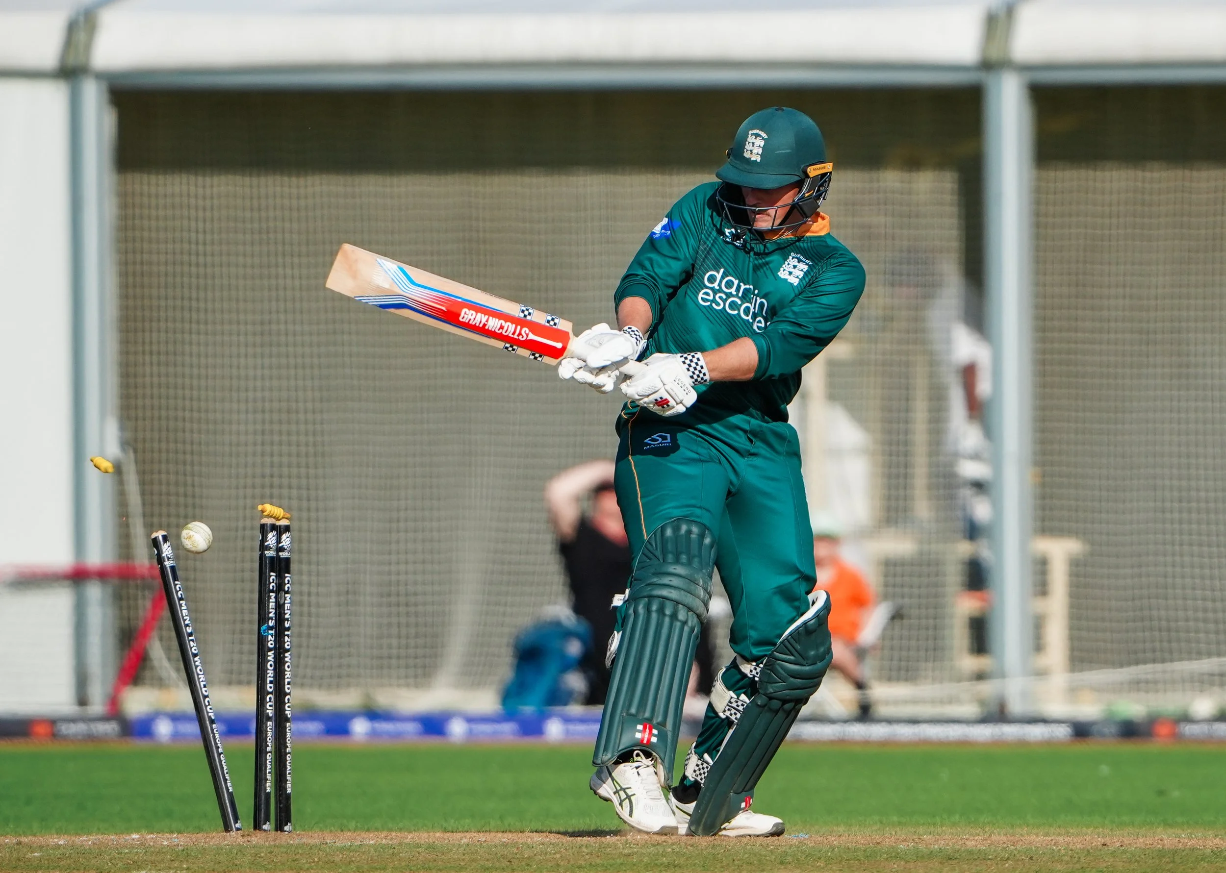 Cricket player in green uniform hitting a cricket ball with a bat during a match.