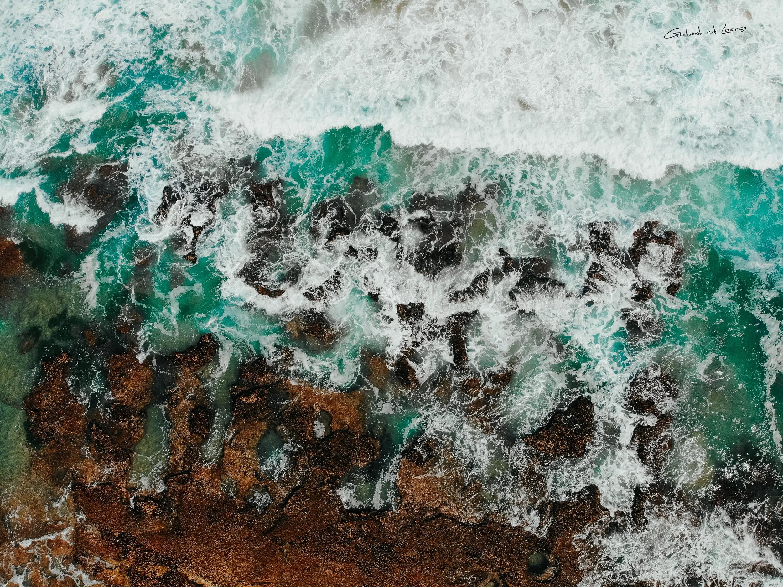 Top-down aerial view of ocean waves crashing over rocks along a shoreline.