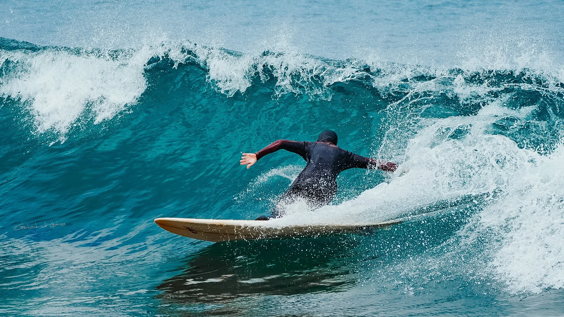 A surfer in a wetsuit riding a large blue wave on a surfboard in the ocean.