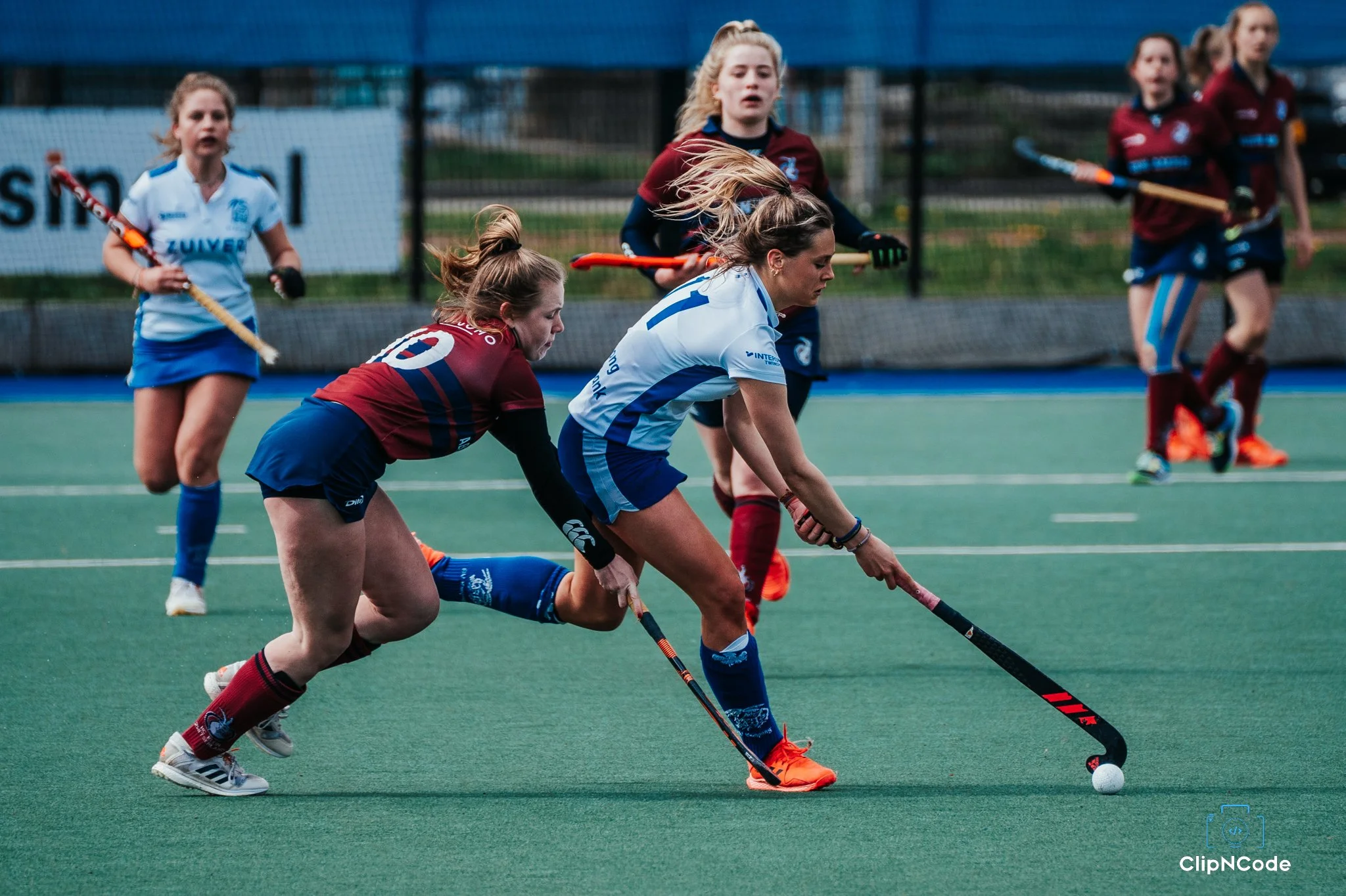 Women playing field hockey, battling for control of the ball on an outdoor sports field