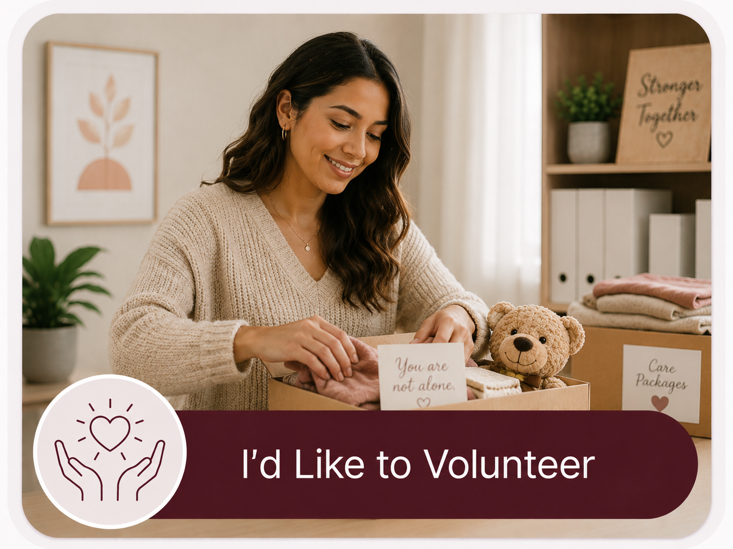 A woman smiling while preparing a care package with a teddy bear, pink socks, and a card that reads 'You are not alone.' on a table in a cozy room with shelves and plants.