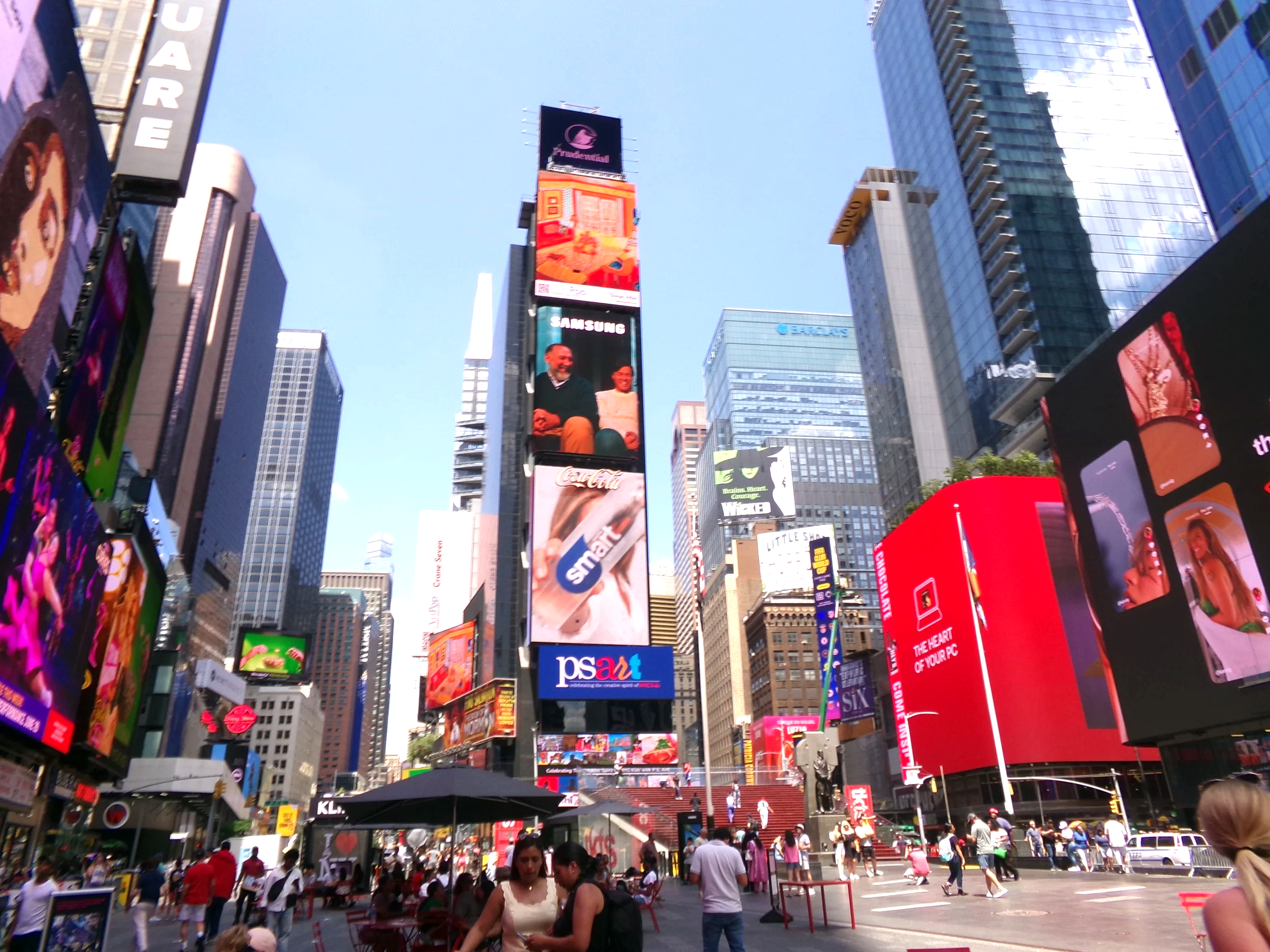 Crowded Times Square in New York City with numerous digital billboards and advertisements on tall buildings, and people walking in the streets.