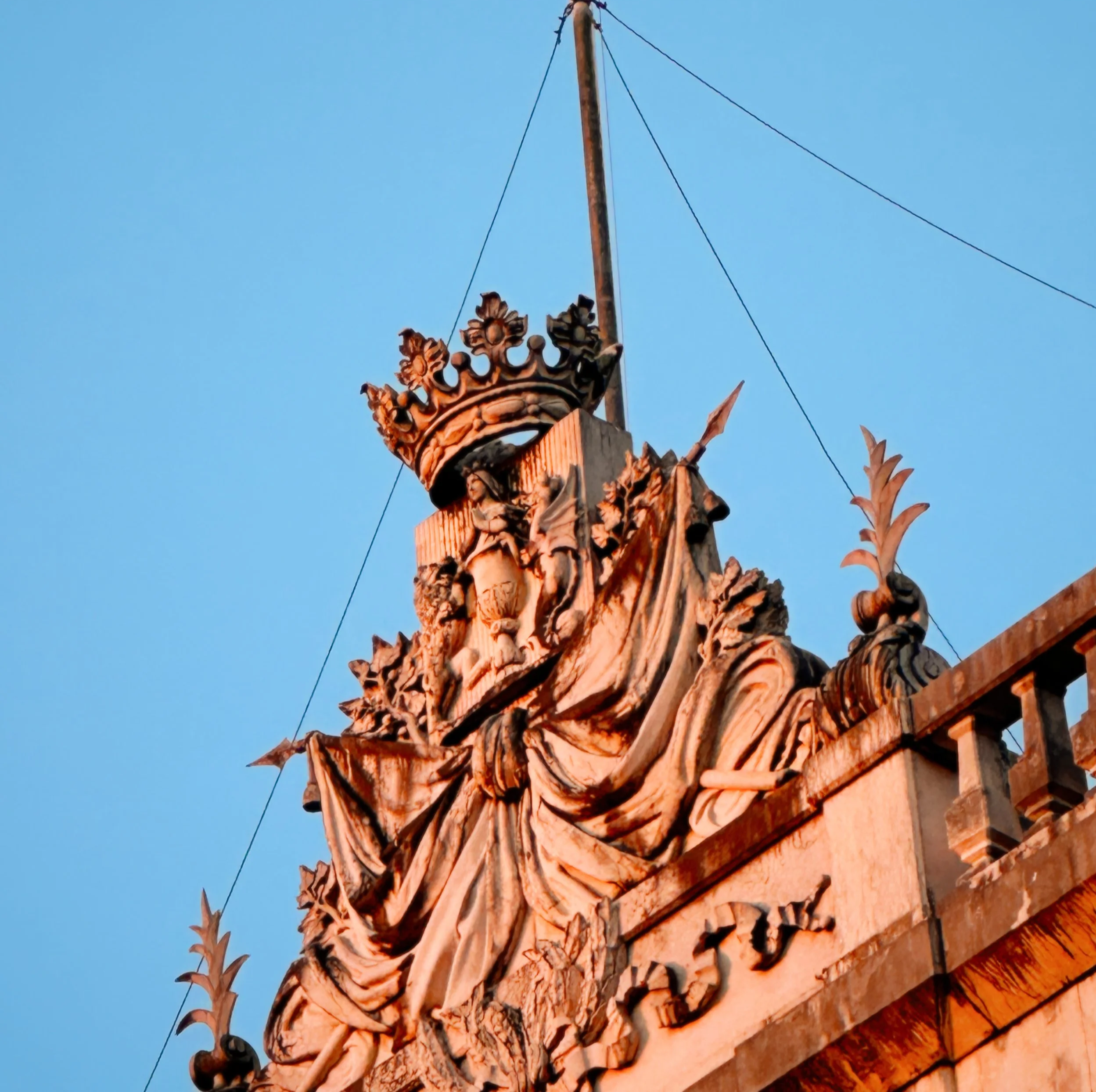 Close-up of an ornate wooden architectural detail on a building, featuring carved woodwork and a decorative crown, set against a clear blue sky.