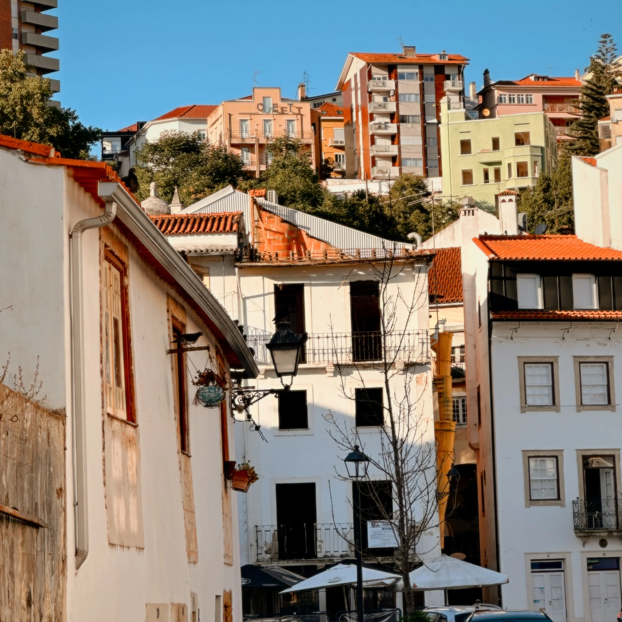 A street scene in a European city with parked cars, narrow cobblestone streets, and multistory residential buildings with balconies on a sunny day.