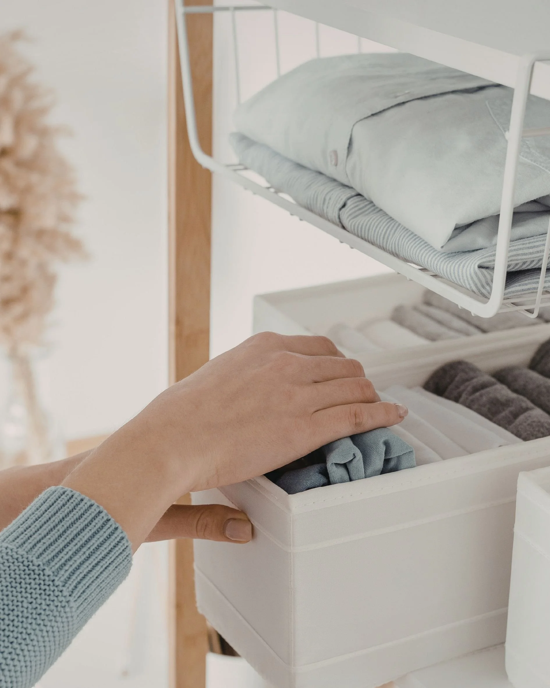Person wearing a blue knitted sweater organizing folded clothes in a white wooden drawer.