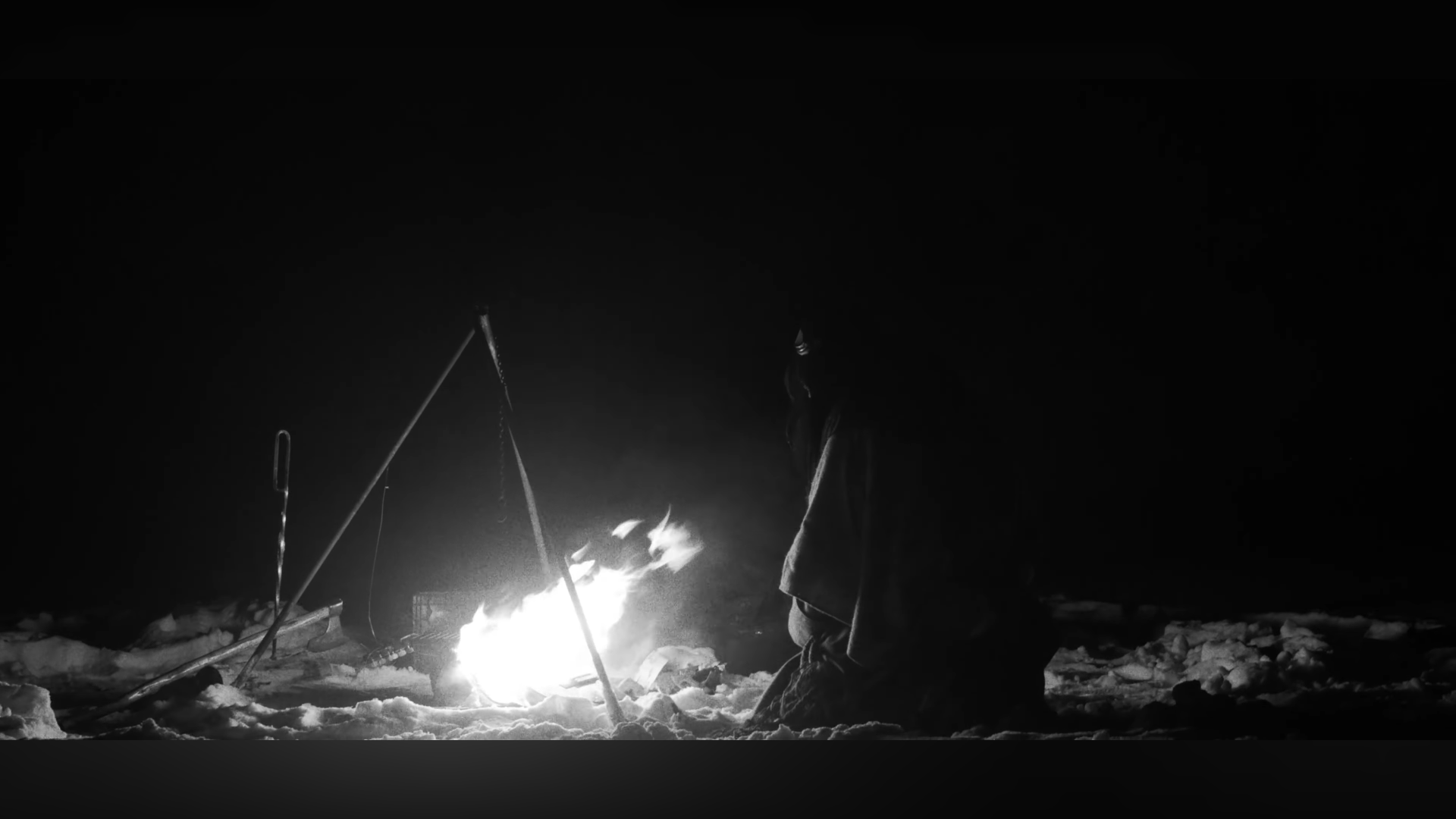 Personne près d'un feu de camp sur la neige, la nuit, tendant un ustensile au-dessus du feu.