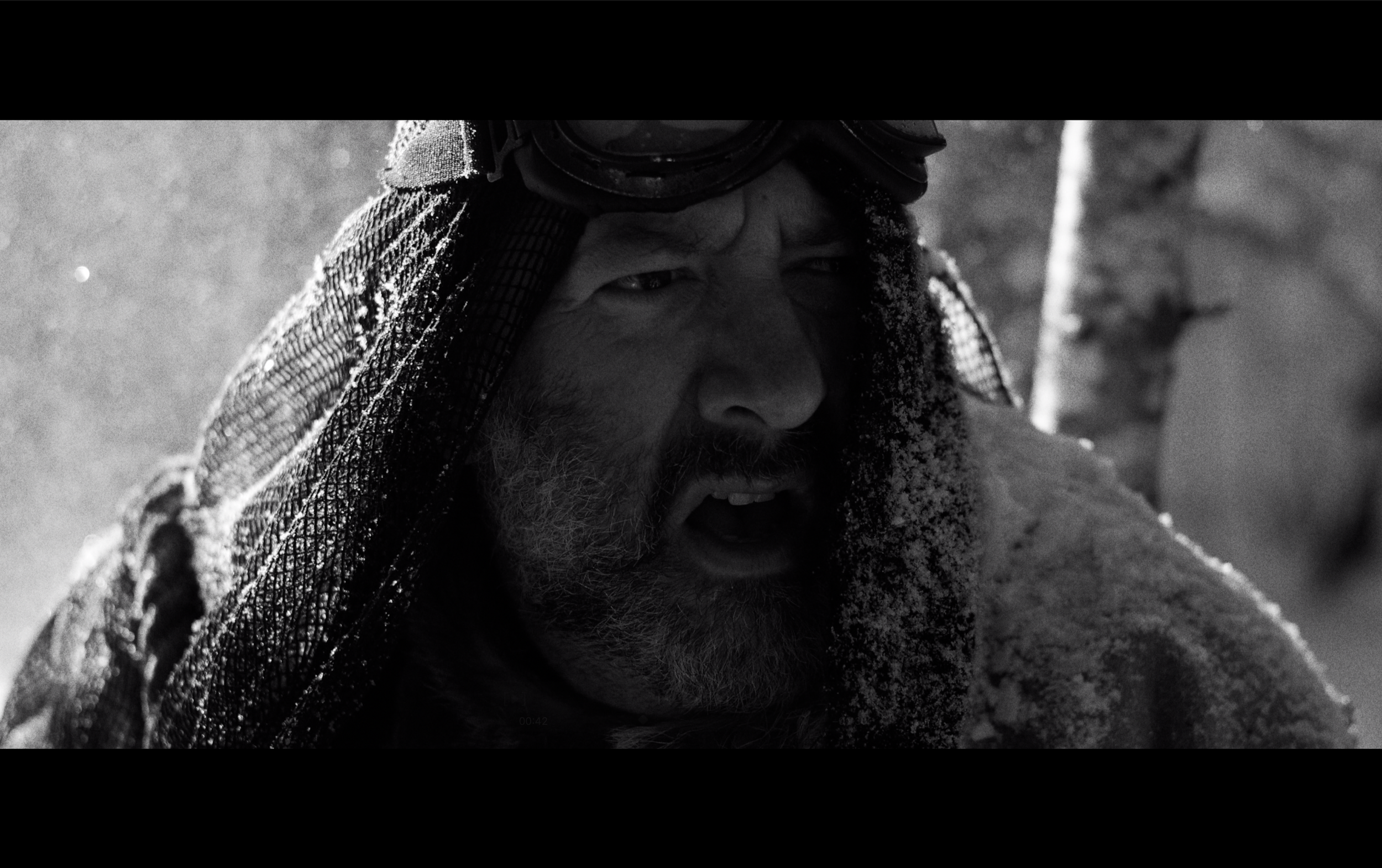 Un homme avec une barbe, portant des lunettes de ski, en situation de froid intense, avec de la neige sur ses vêtements et son visage.