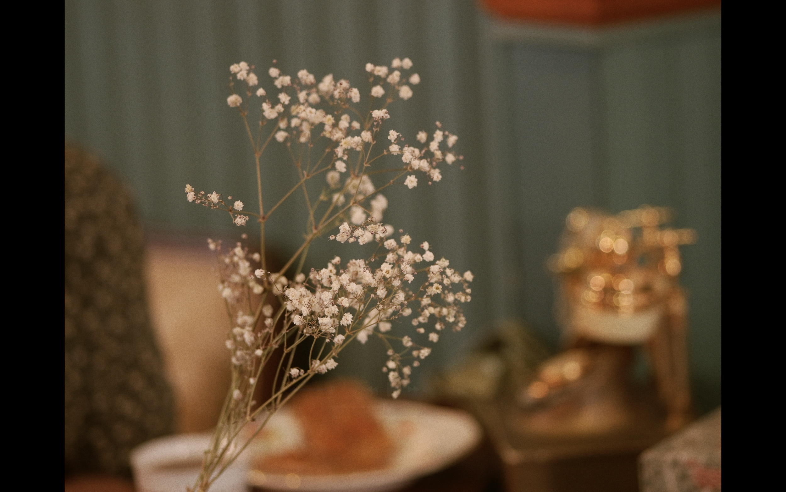 Raisinée de petites fleurs blanches dans un vase, avec un fond flou montrant des objets dorés et des plats.