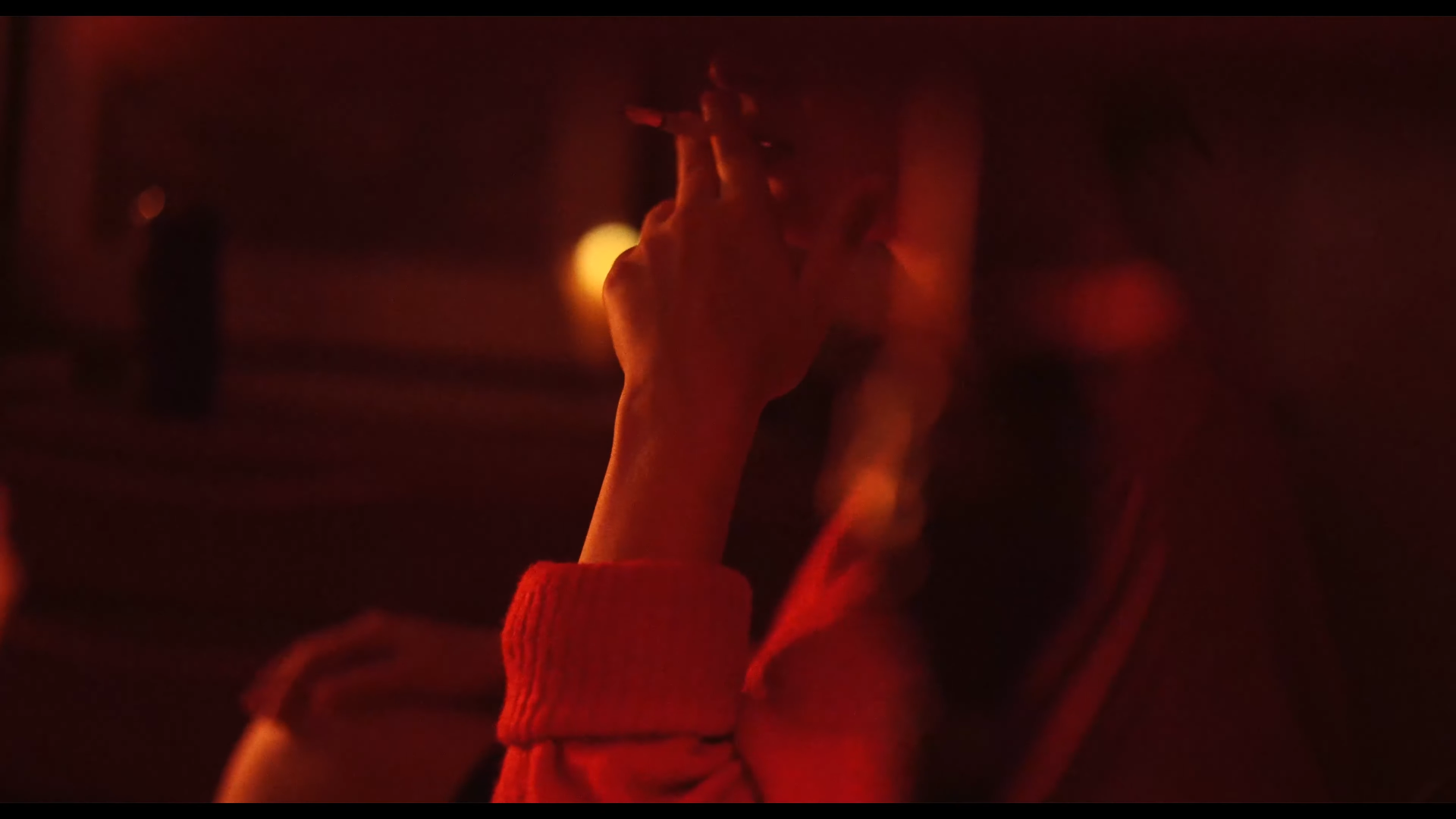 Une personne avec une main levée, faisant un signe de paix, dans un environnement sombre avec une lumière rougeâtre