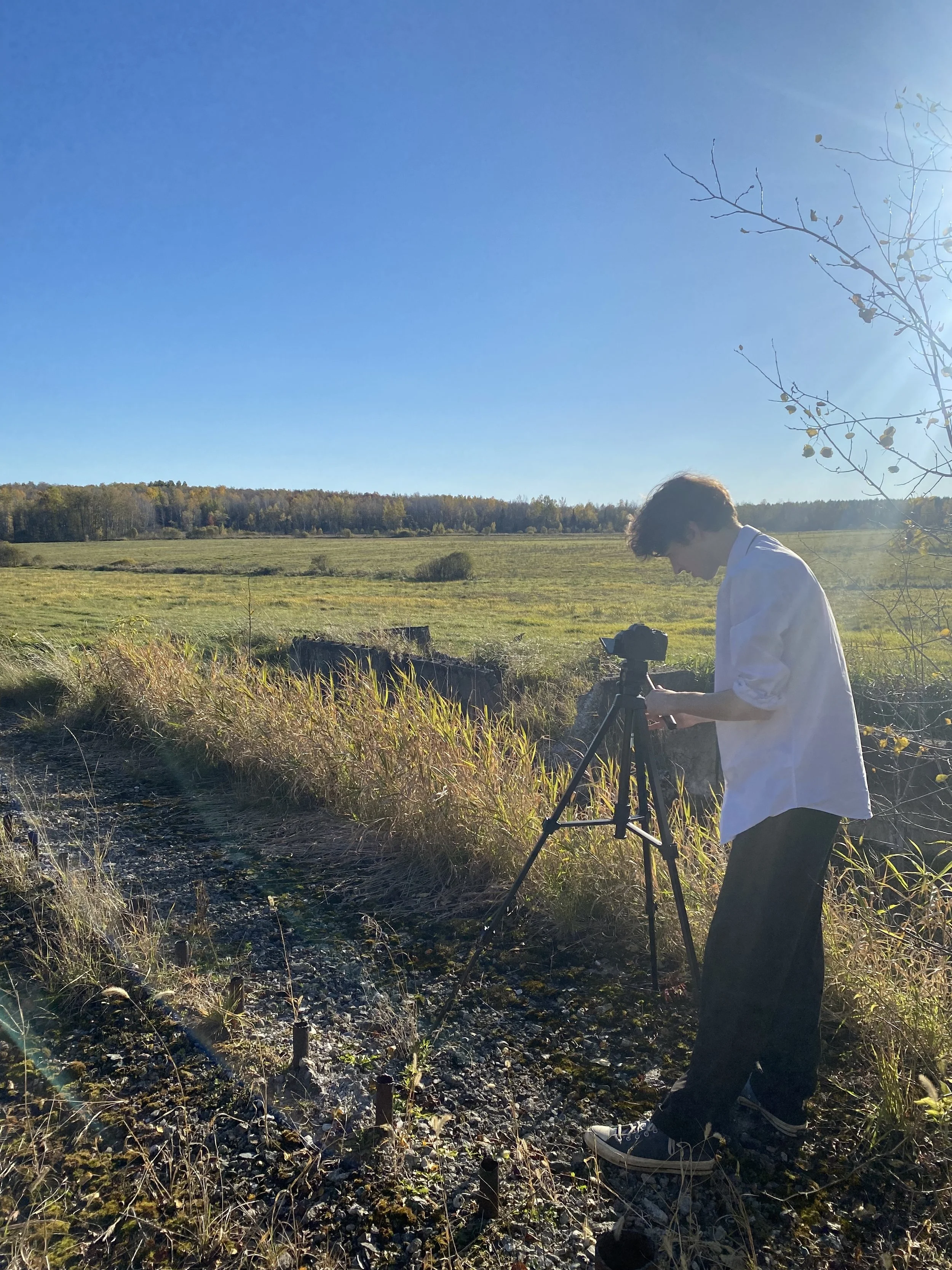 Un jeune homme utilise un appareil photo monté sur un trépied dans un champ lors d'une journée ensoleillée.