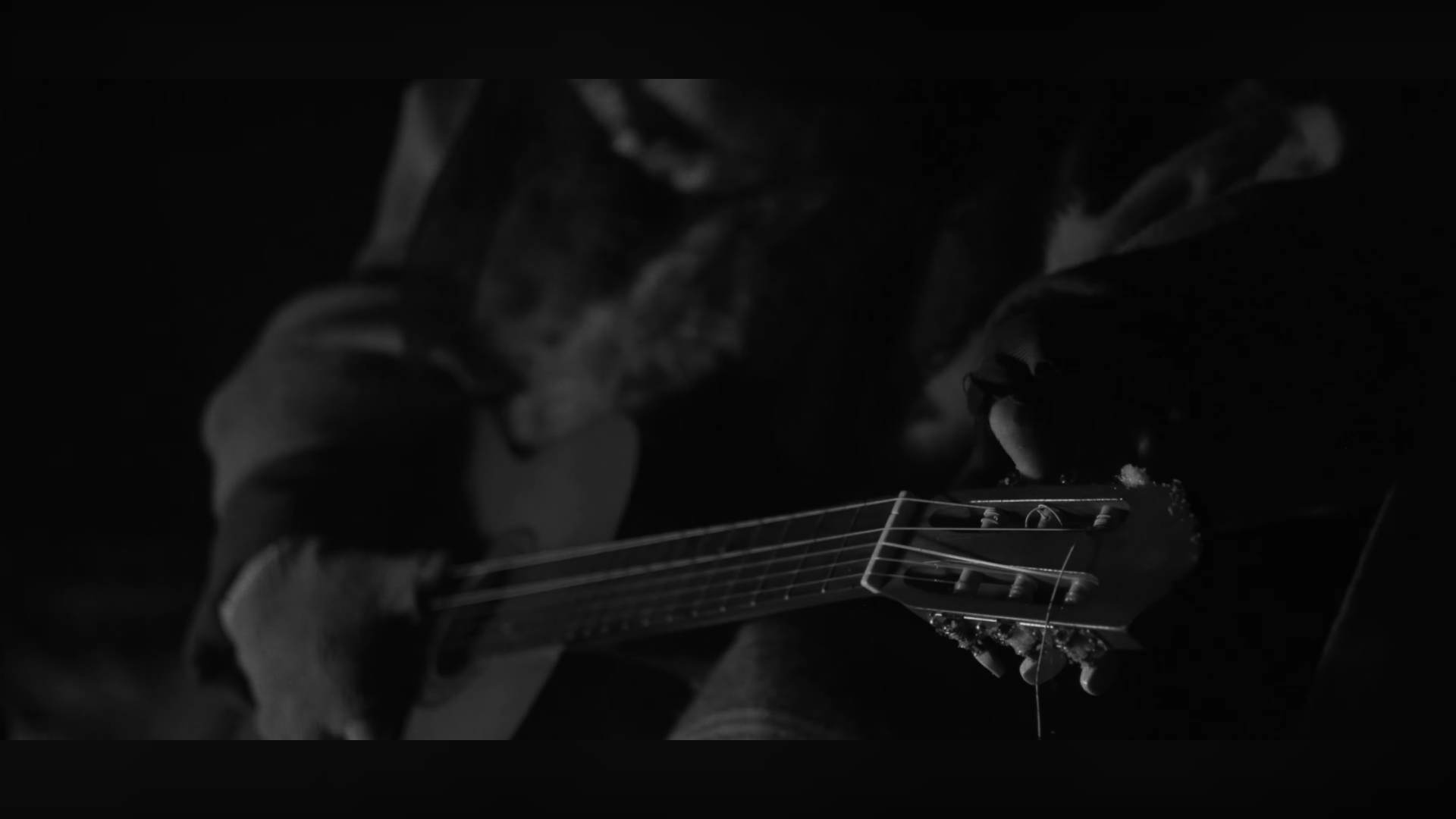 Gros plan d'une personne jouant de la guitare acoustique, en noir et blanc, avec des détails sur la tête de la guitare et les mains de l'artiste