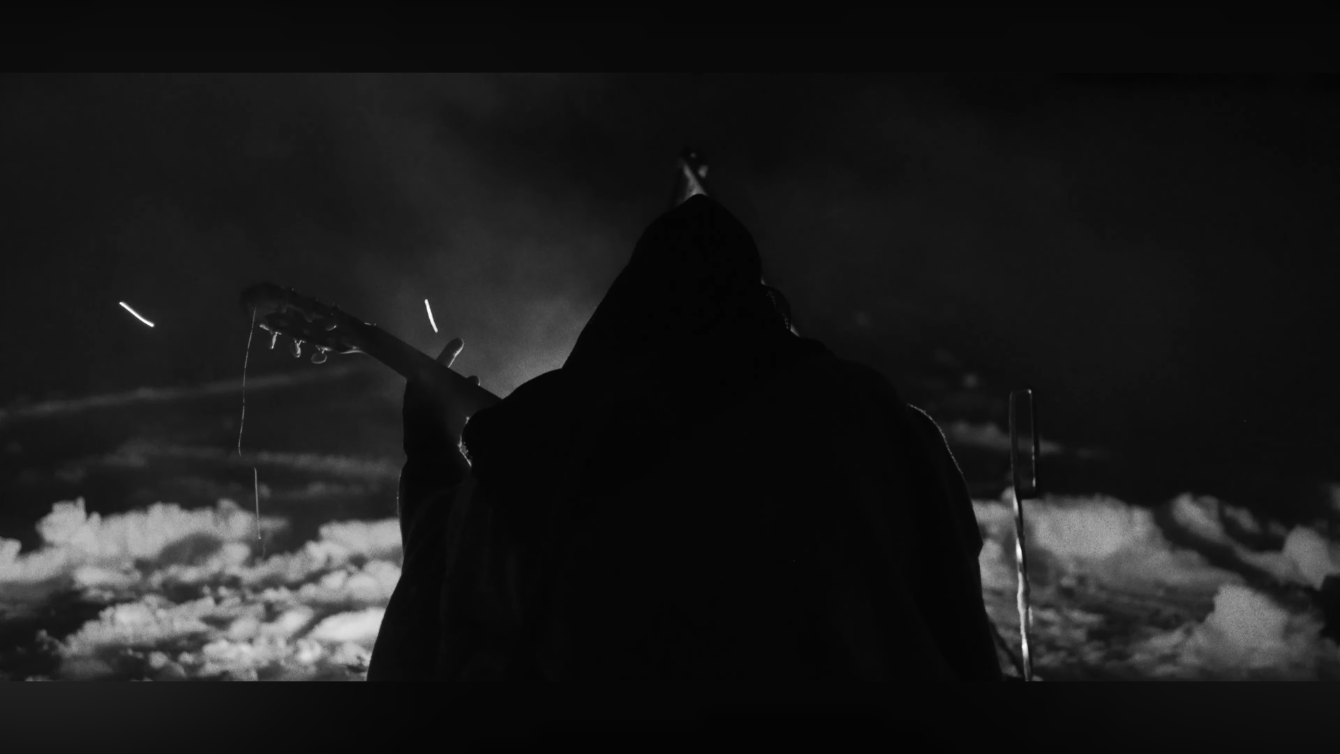 Silhouette d'une personne jouant de la guitare dans un paysage enneigé sombre, avec un ciel nuageux.