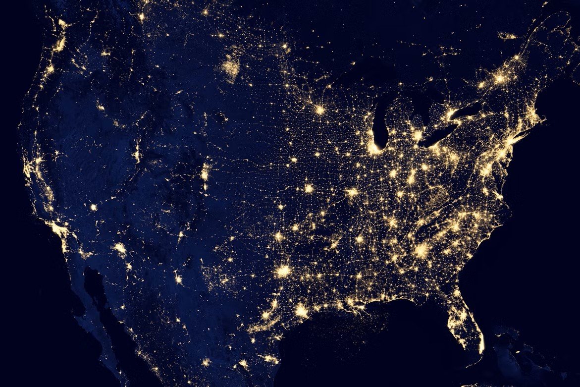 Satellite view of the United States at night showing city lights and illuminated areas.