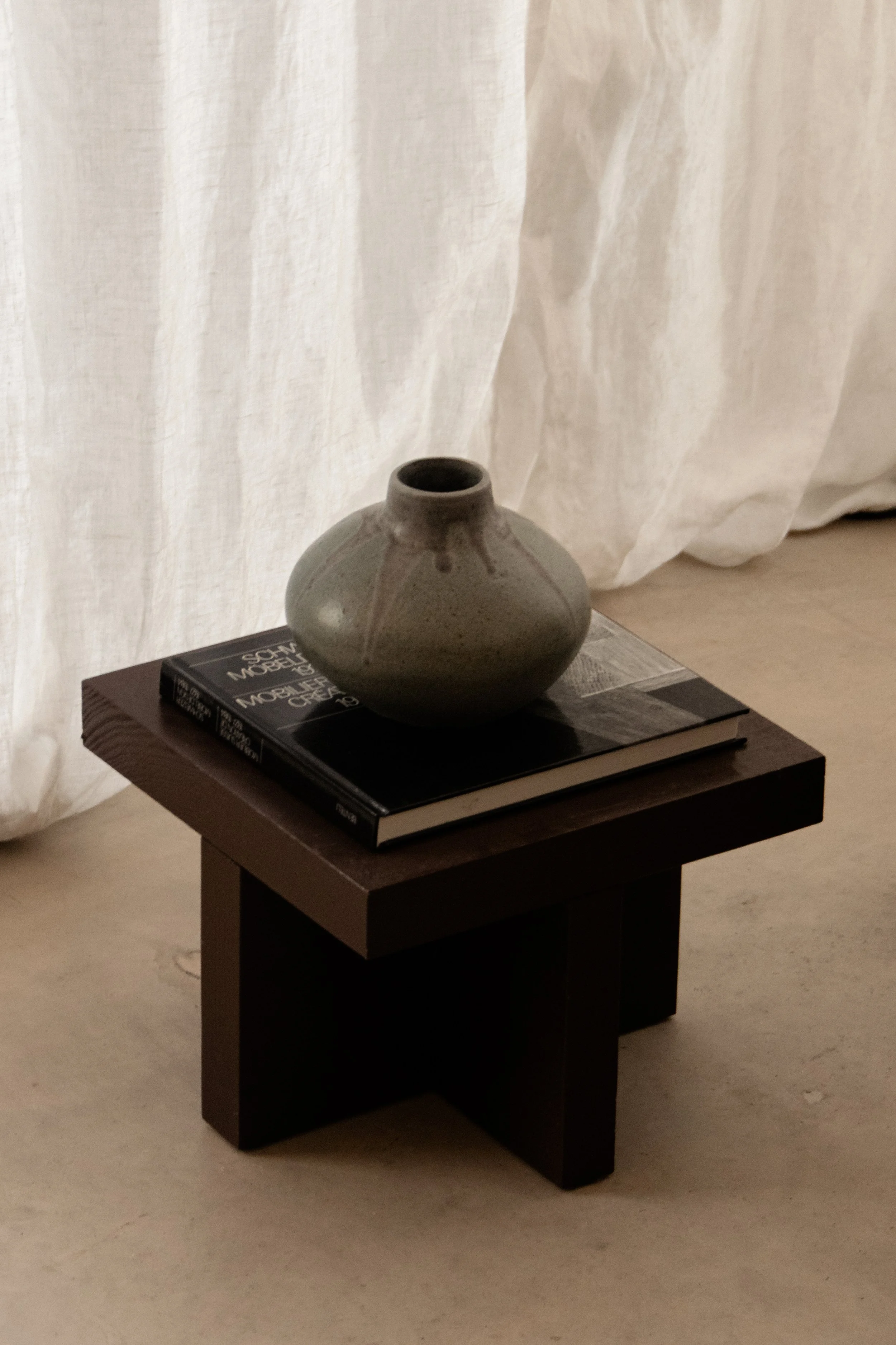 Ceramic object styling on sculptural dark wood side table with linen backdrop