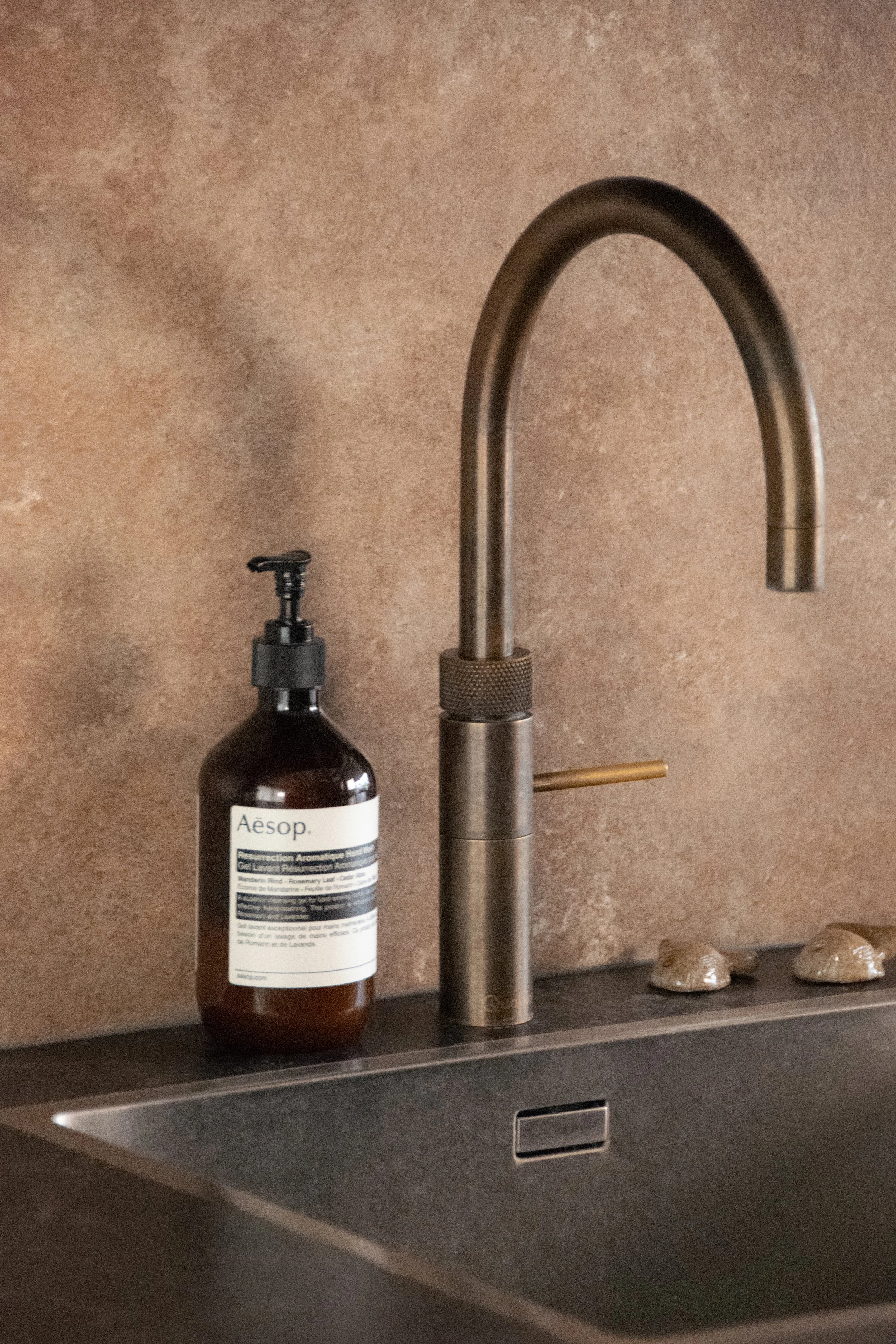 Kitchen sink detail with brushed metal faucet and textured backsplash