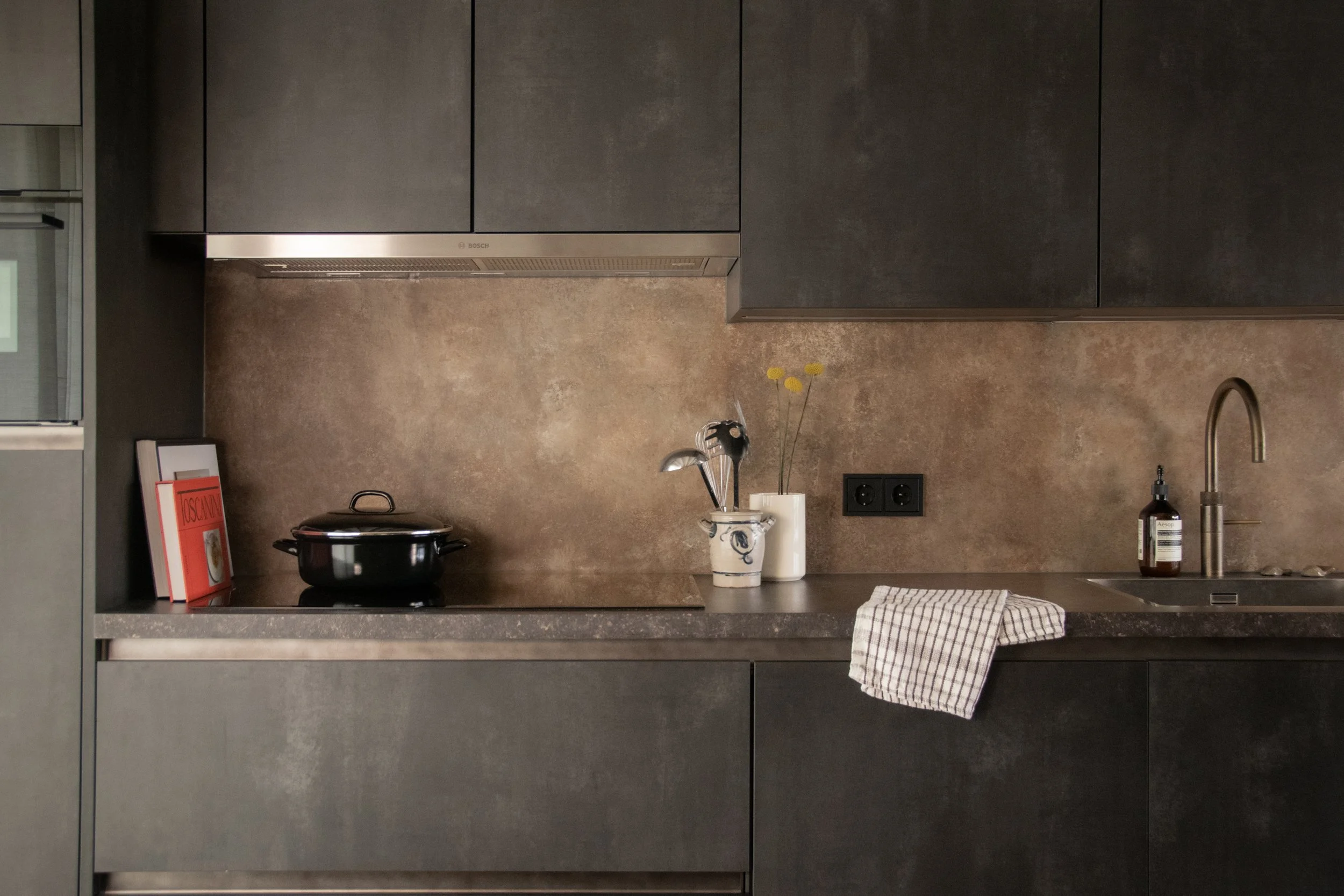 Dark kitchen cabinetry with textured backsplash and warm material palette