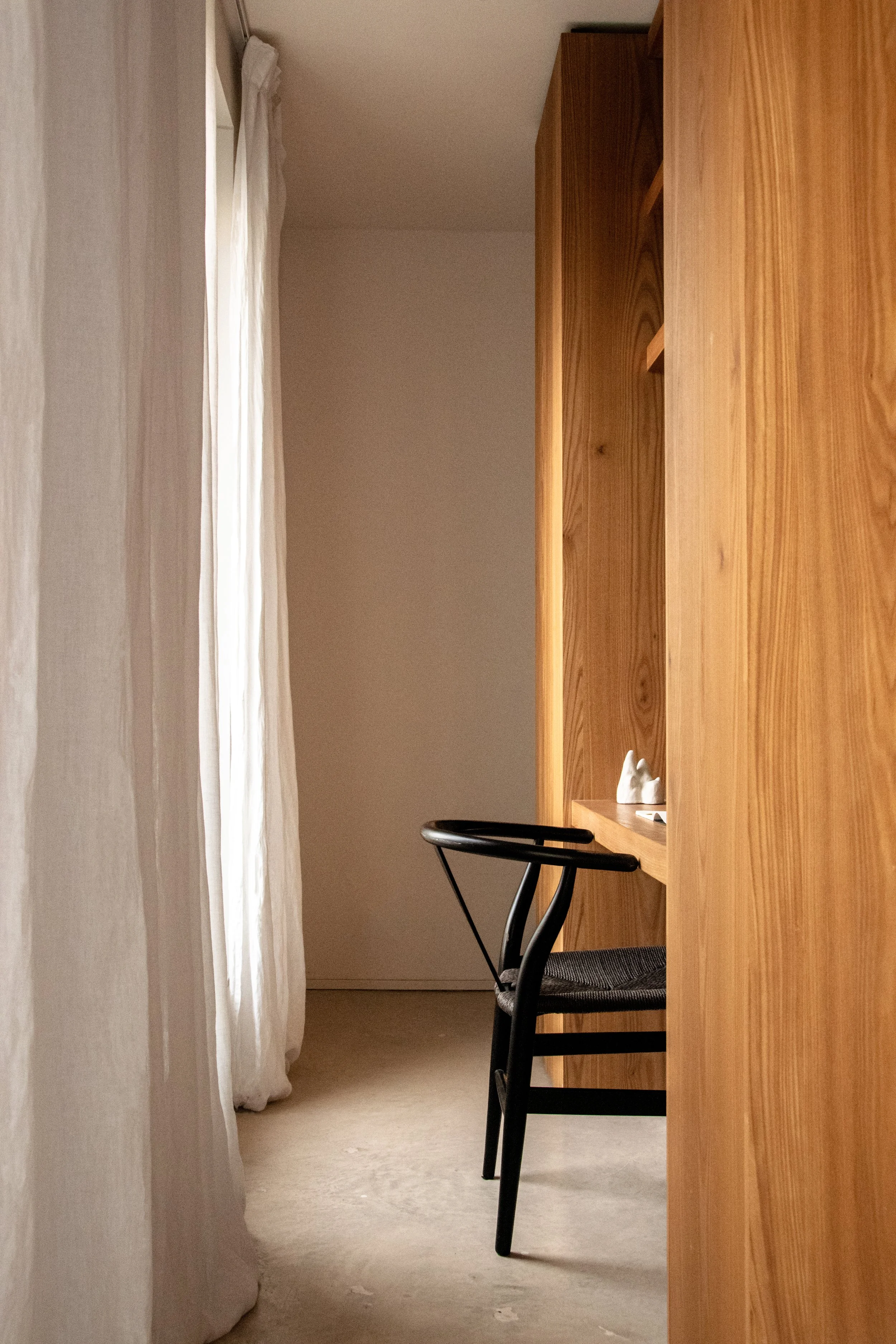 Workspace nook with oak cabinetry, linen curtains and sculptural chair in Antwerp apartment