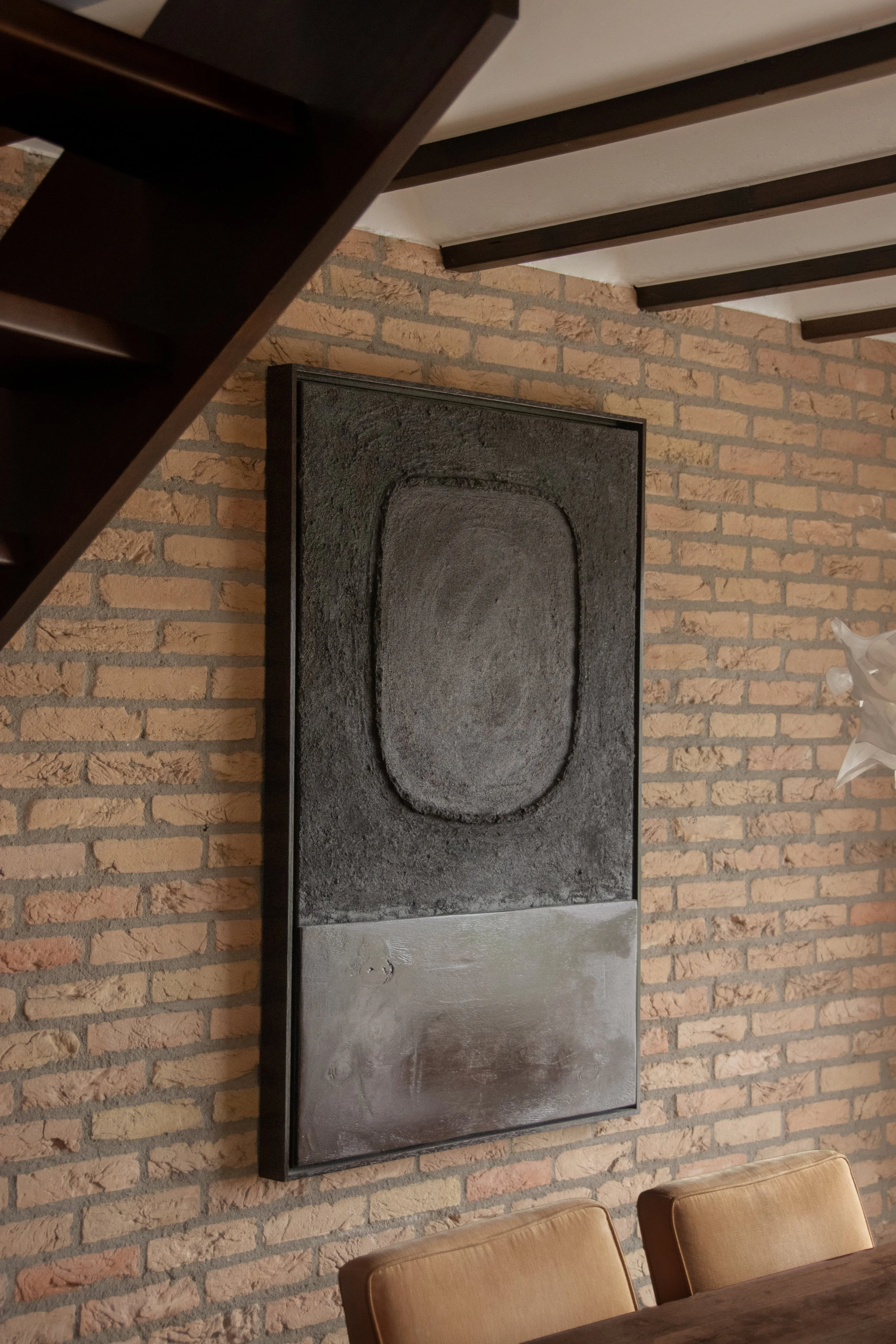 Large textured artwork above dining chairs against exposed brick wall
