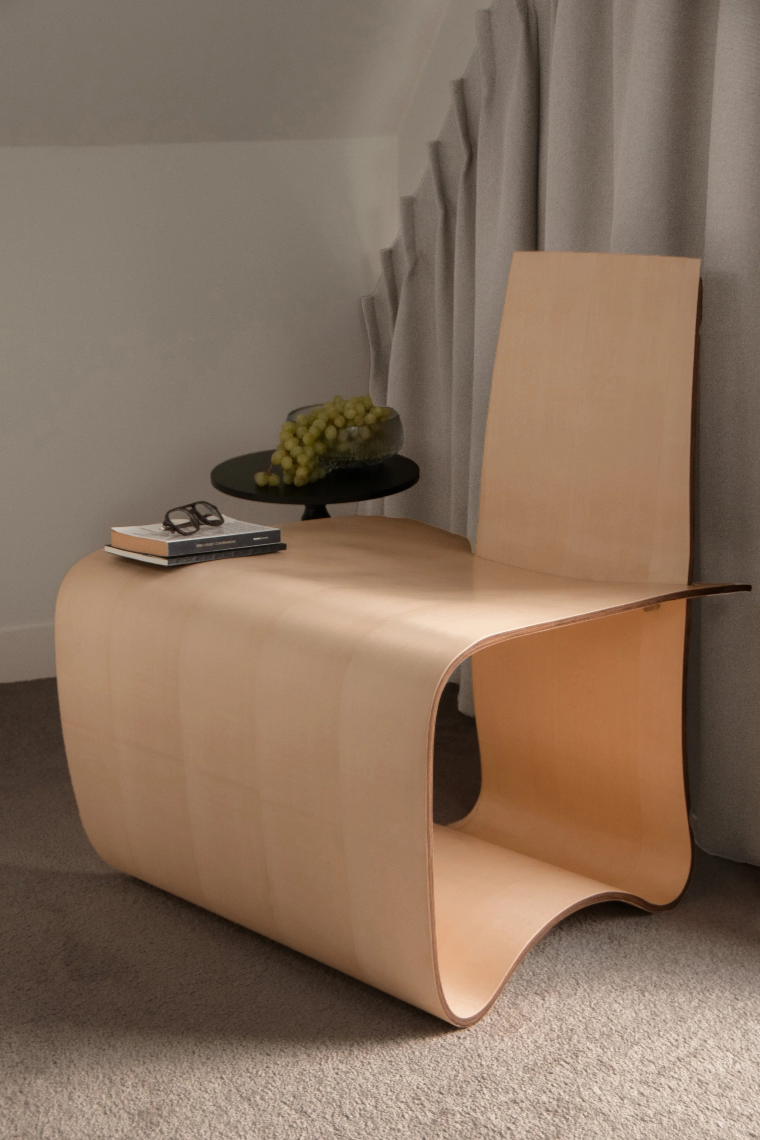 Sculptural curved plywood chair with side table and styled objects
