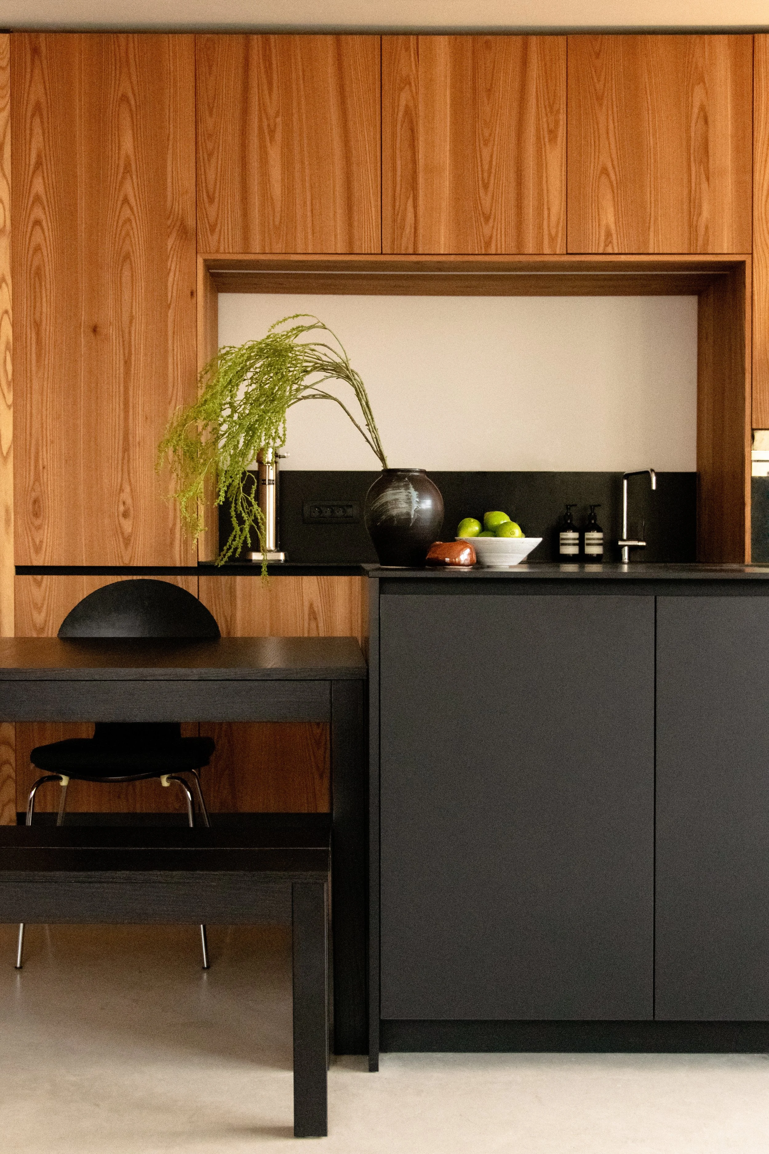 Kitchen with warm oak cabinetry, dark island and integrated dining area in Antwerp apartment