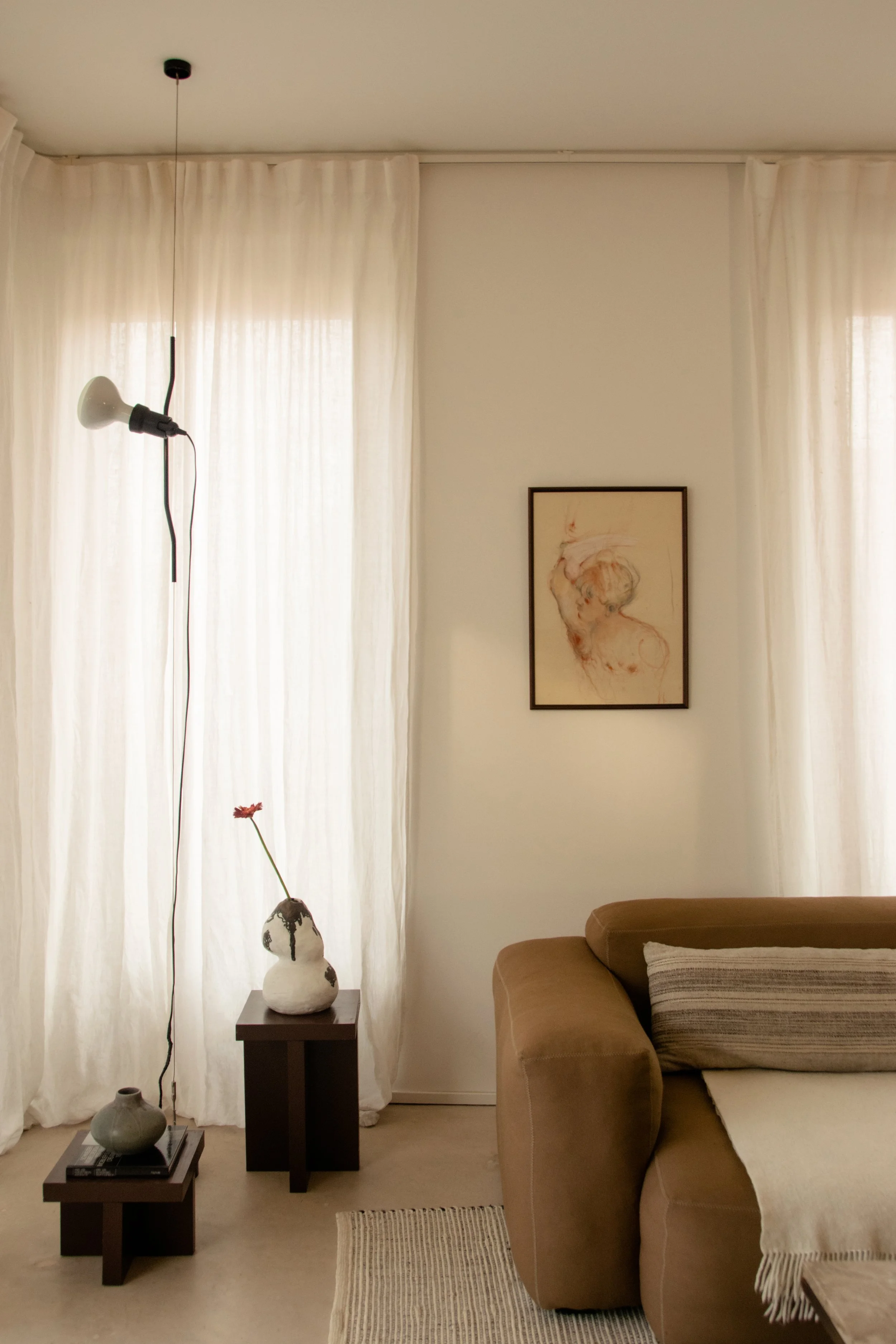 Contemporary living room with linen curtains, warm brown sofa and sculptural styling objects in Antwerp apartment