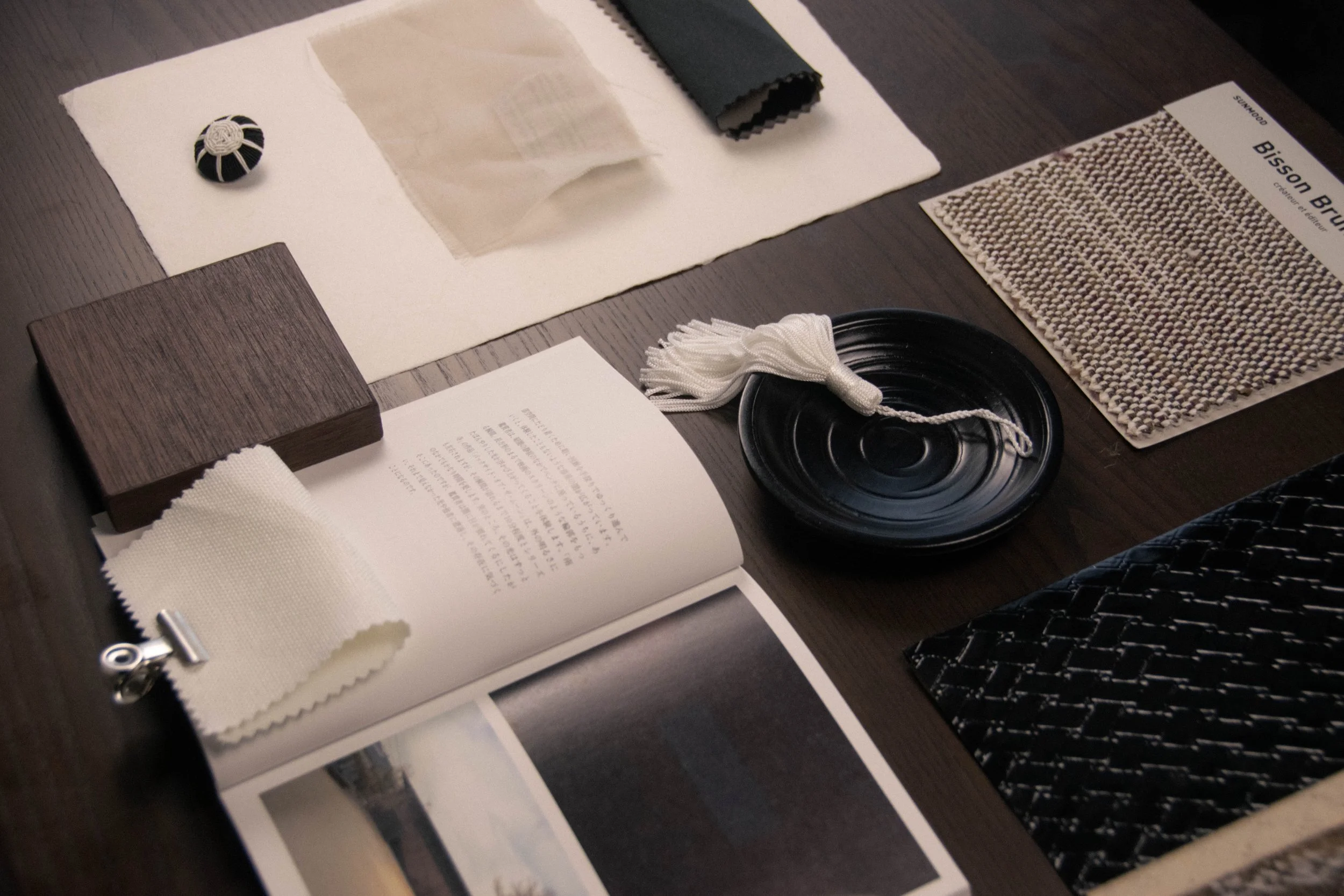 Close-up of fabric and material samples, including a woven textile swatch book and black lacquered dish, from a Studio Cér material palette.