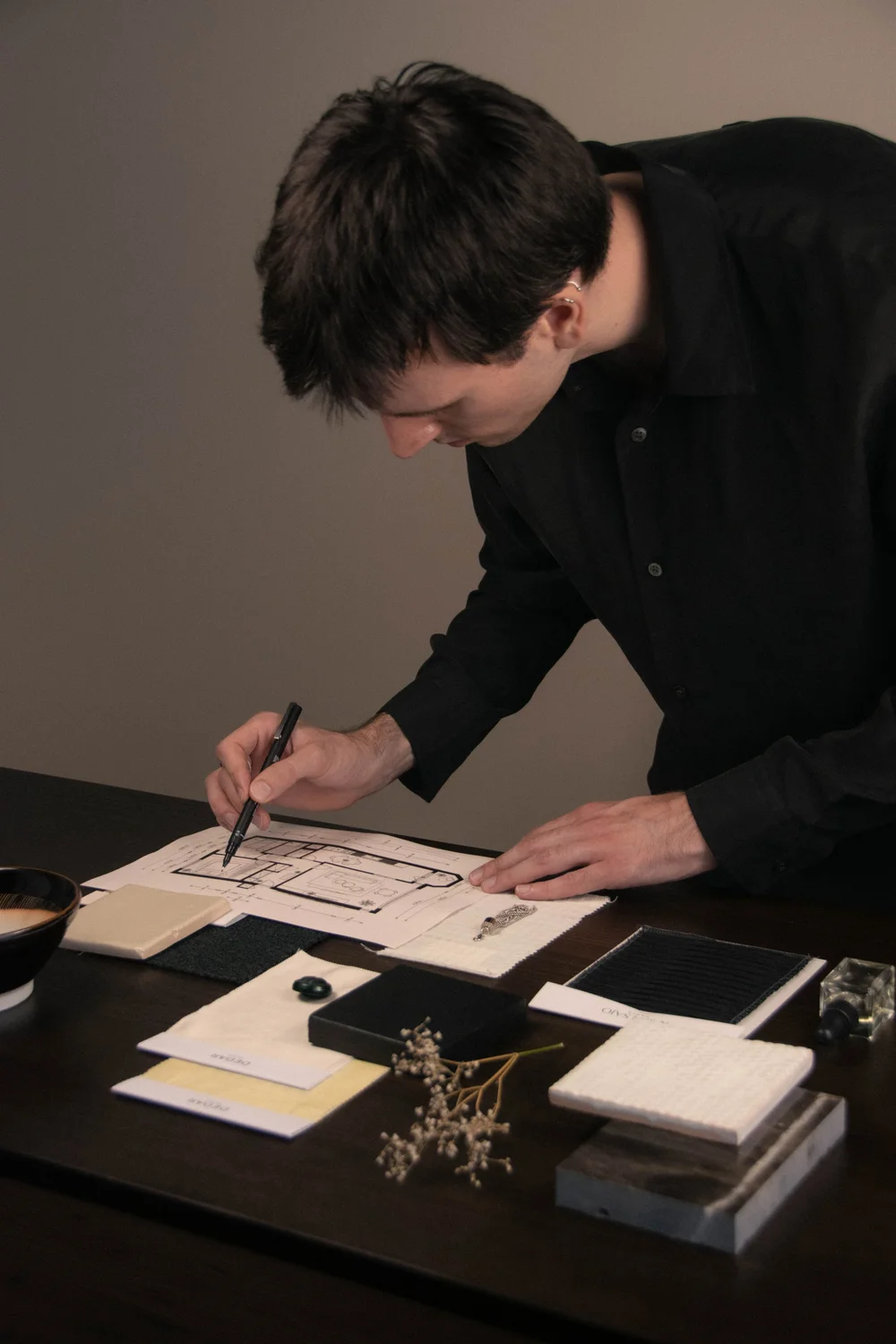 Joost Laméris of Studio Cér sketching a floor plan by hand, surrounded by material and finish samples for a full service interior project.