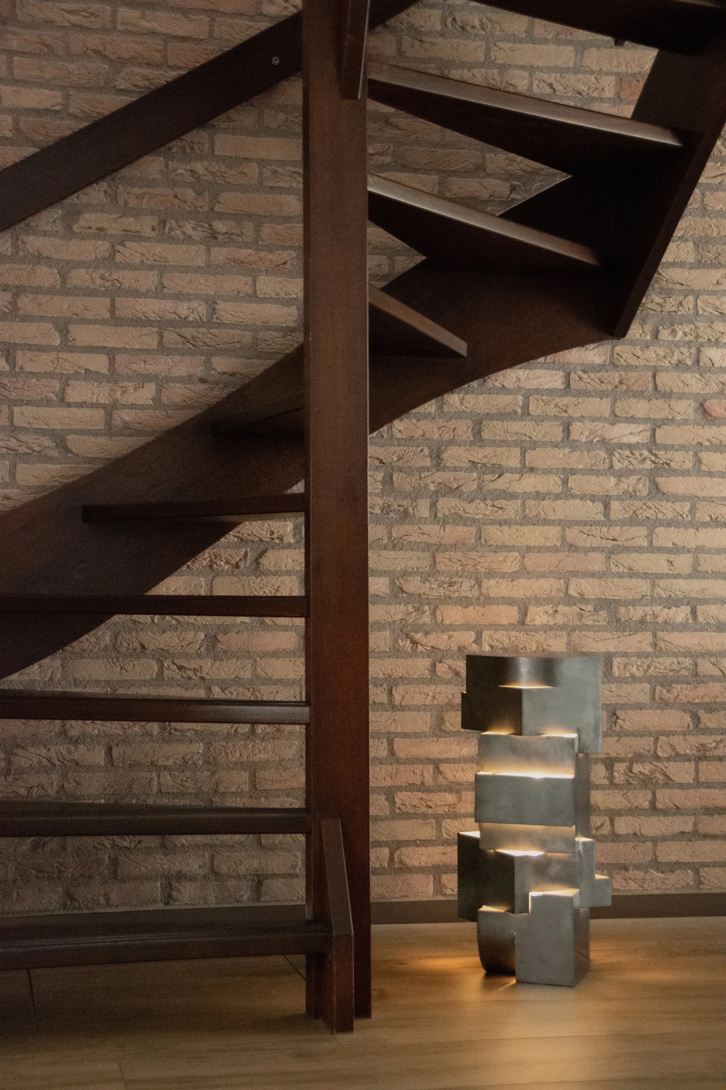 Dark timber staircase against textured brick walls with sculptural floor lighting in the Friesland country home
