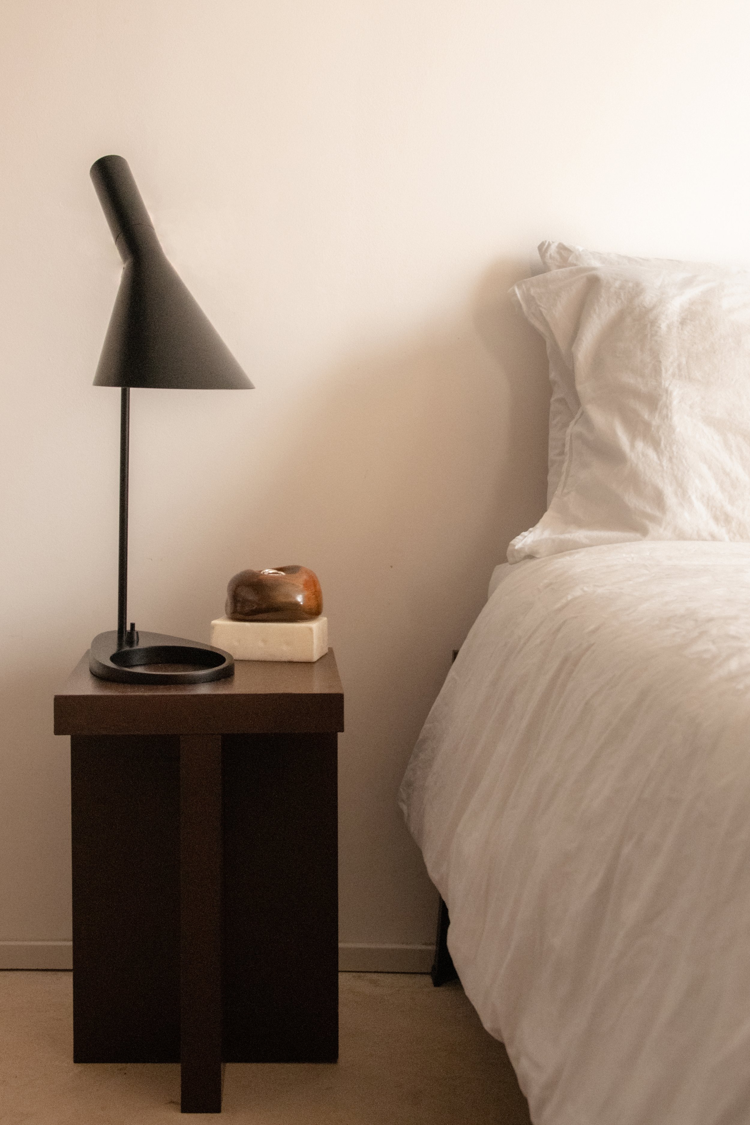 Minimal bedroom with dark wood bedside table, black lamp and soft linen bedding