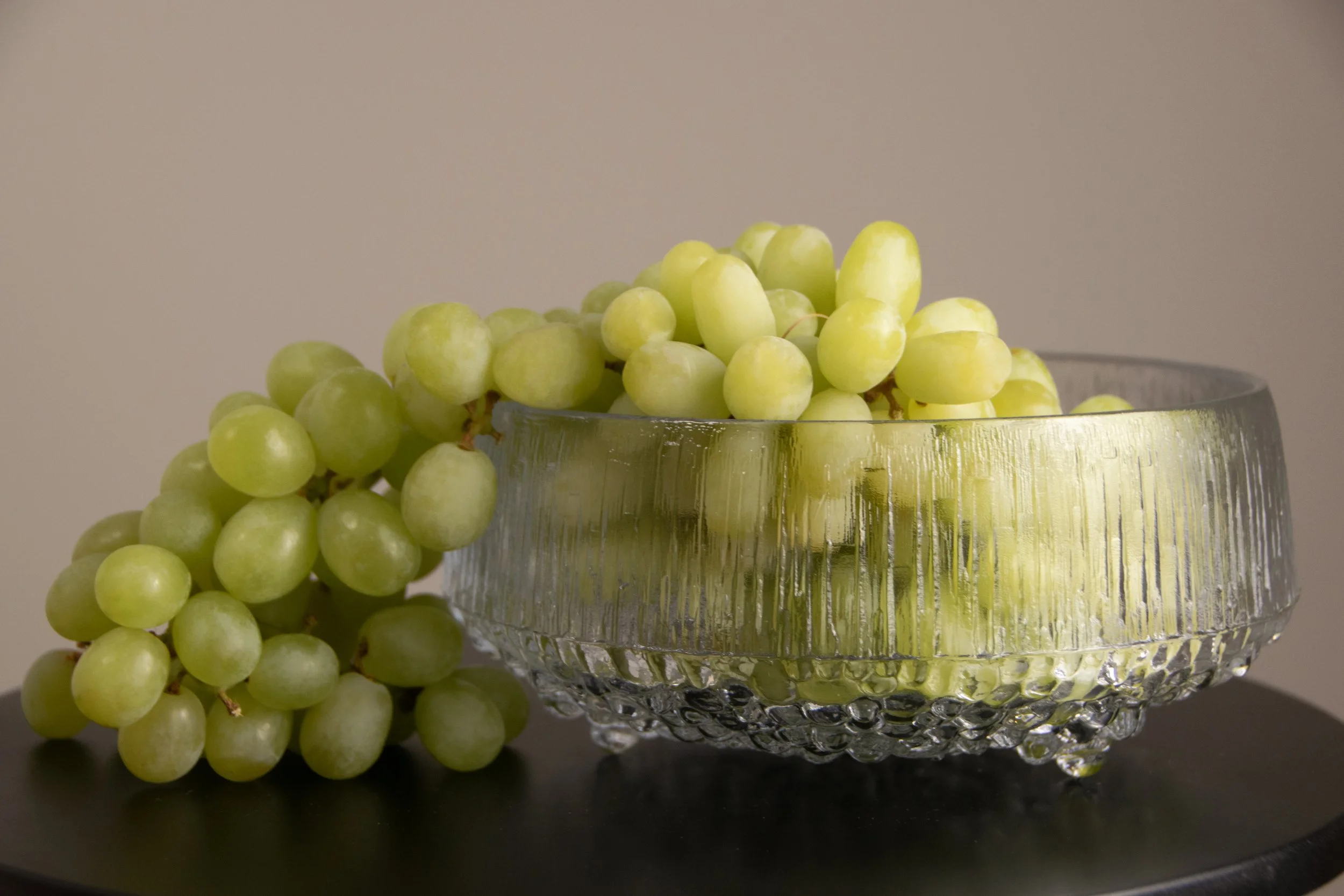 Glass bowl with green grapes styled on a dark table surface