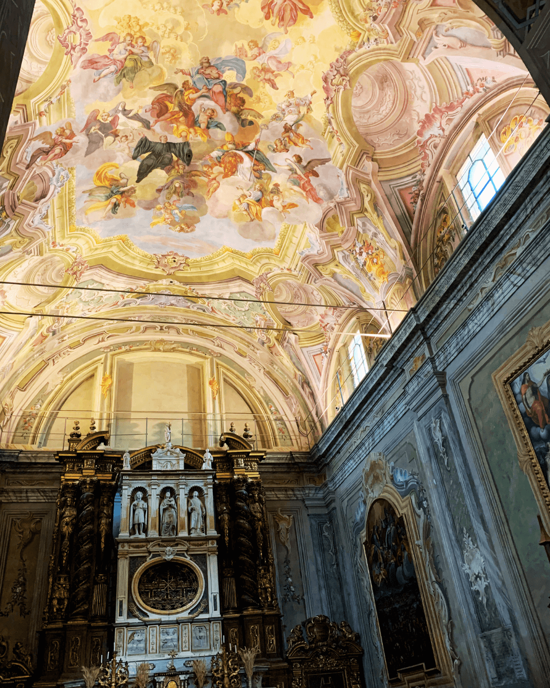 Baroque church interior with a painted ceiling featuring angels and divine figures, along with ornate architectural details and an elaborate altar.