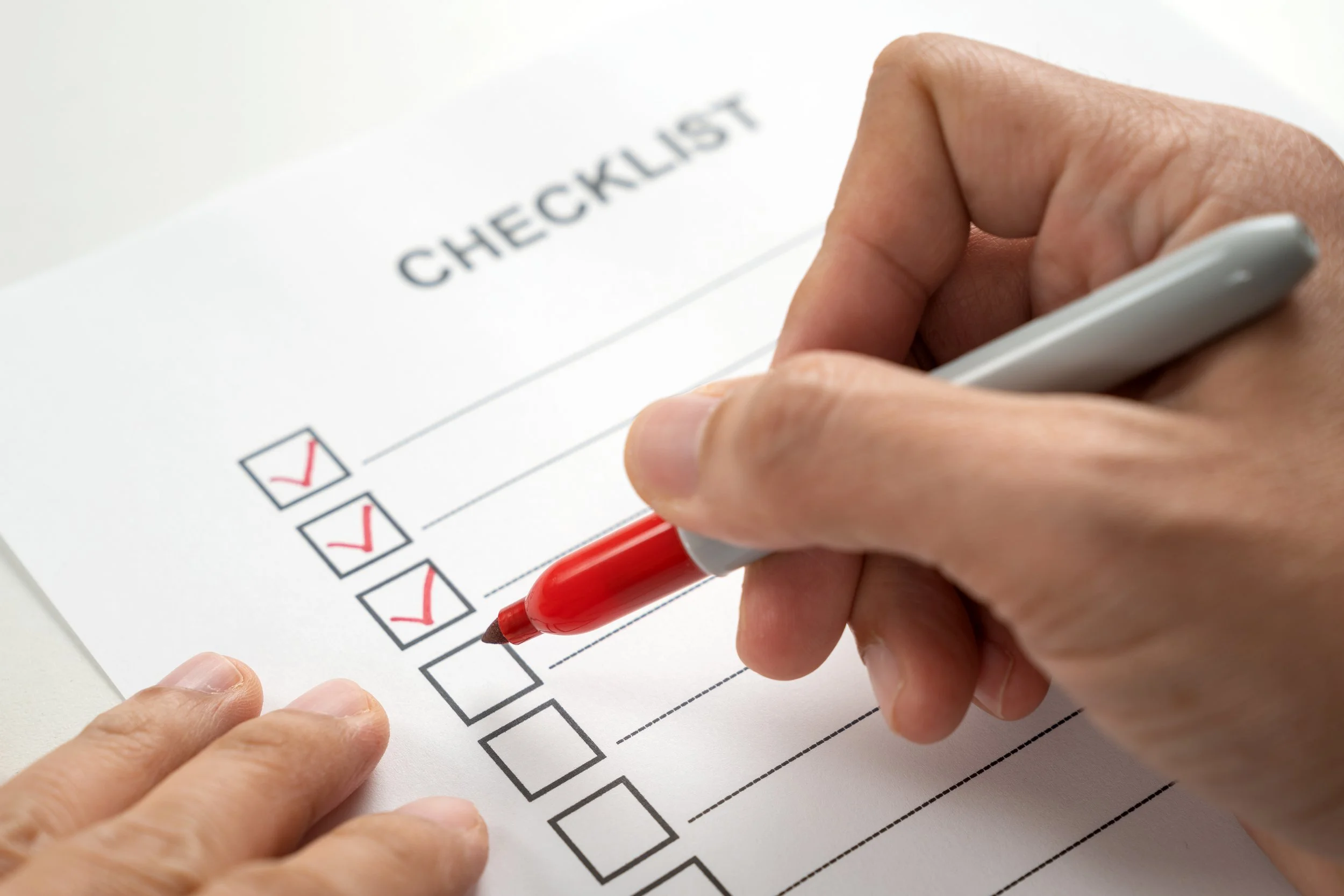 Person checking off items on a checklist labeled 'CHECKLIST' on a white paper with red check marks.
