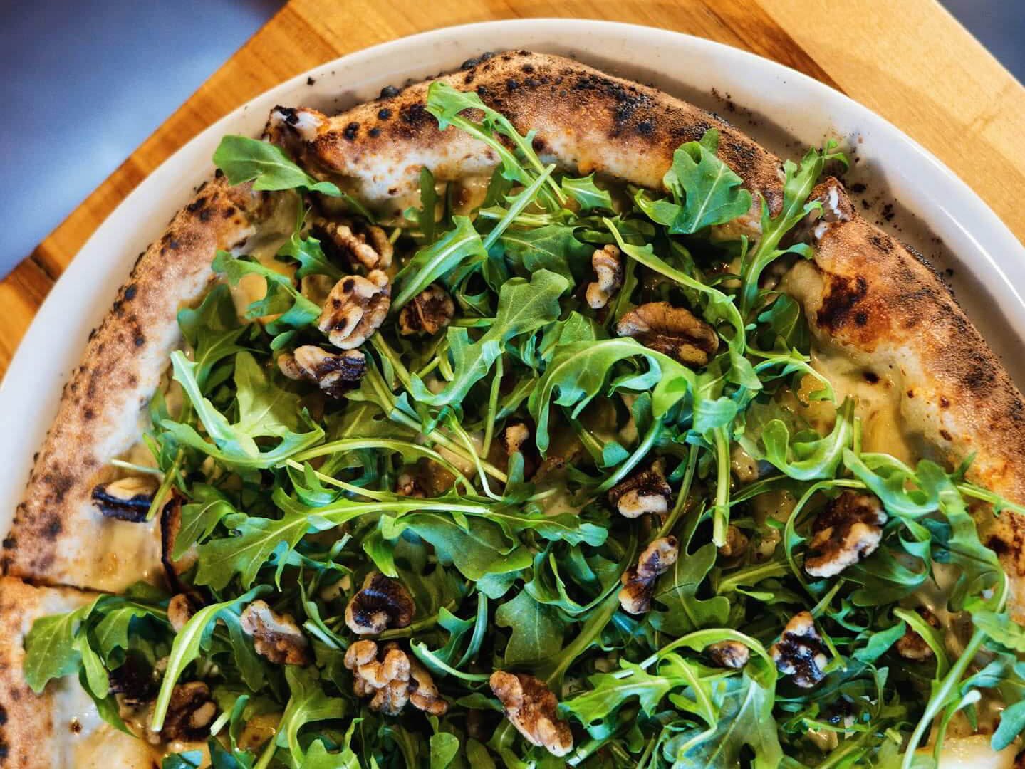 A pizza topped with arugula and chopped walnuts.