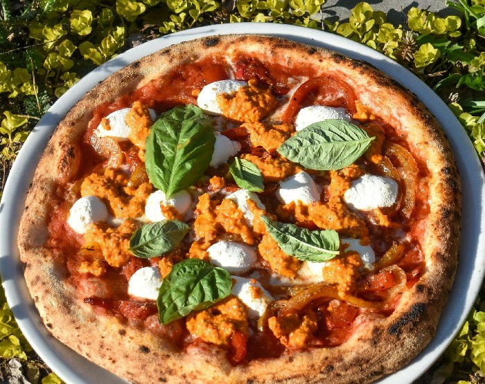 Pizza with tomato sauce, cheese, roasted red peppers, Calabrian pepper pesto, and fresh basil.