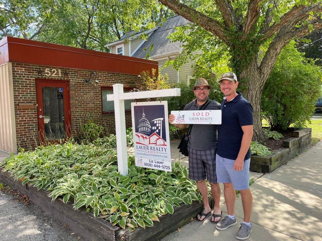 Chris and Alessandro standing in front of the pizzeria holding a "sold" real estate sign