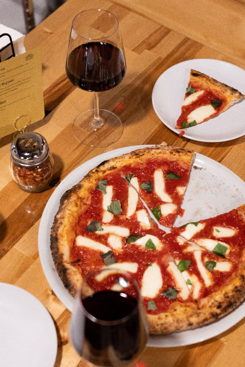 Top-down view of a pizzeria table with a margherita pizza and glasses of red wine