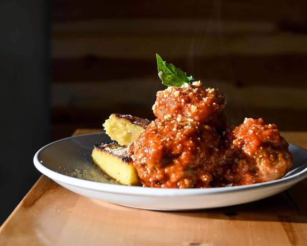Plate of three meatballs covered in tomato-meatball sauce, served with fried polenta wedges.