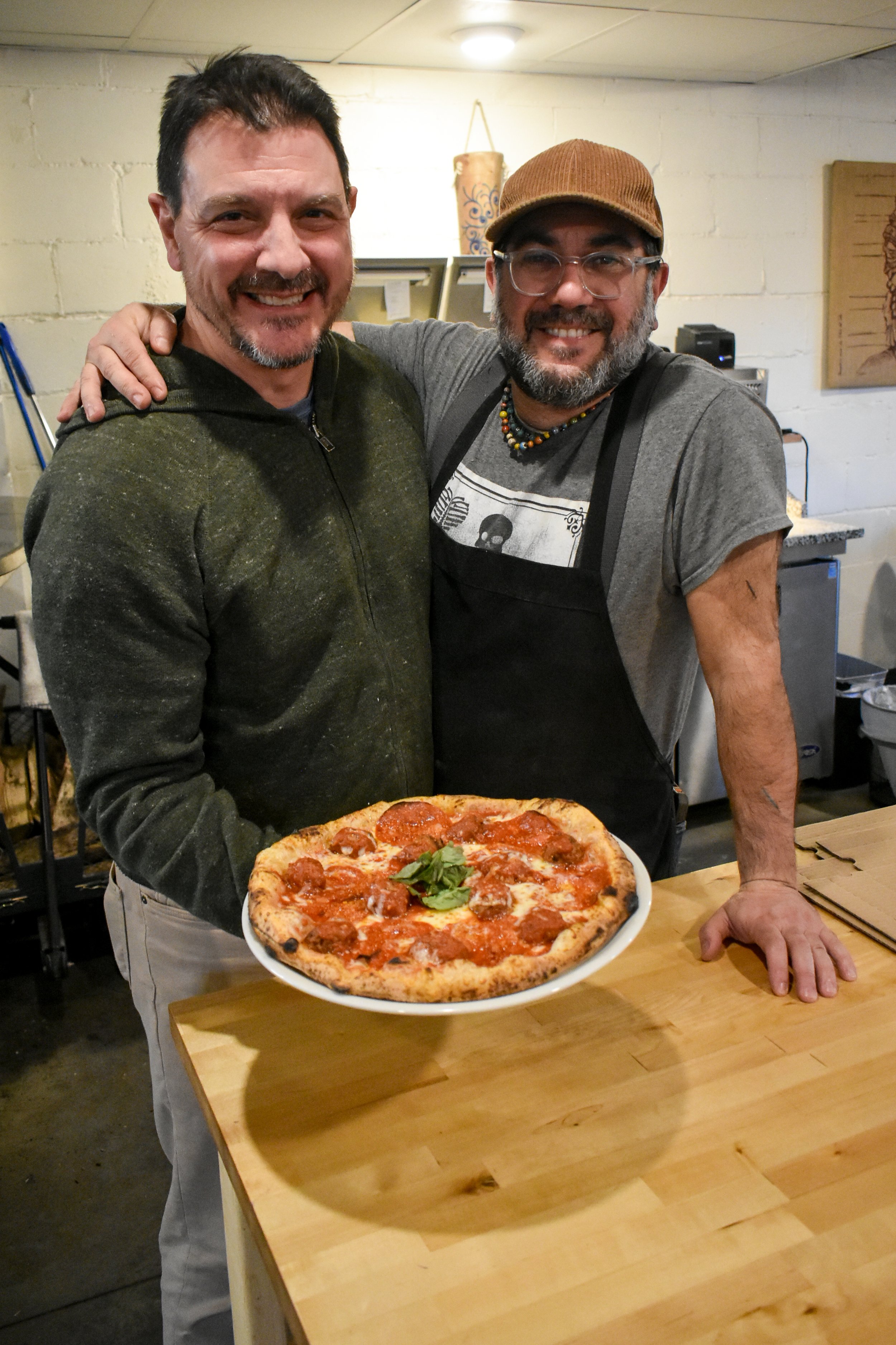 Chris and Alessandro standing inside the pizzeria with their arms around each other