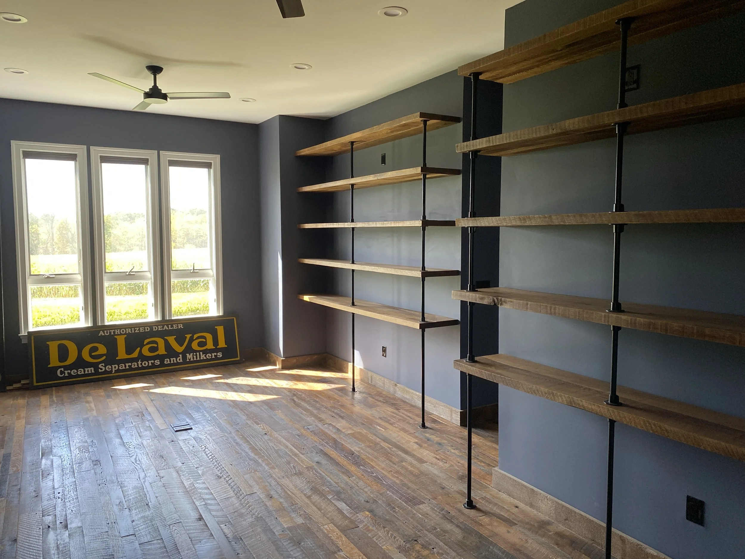 Office room with large windows, wooden floors, and white oak wooden shelves on the wall.