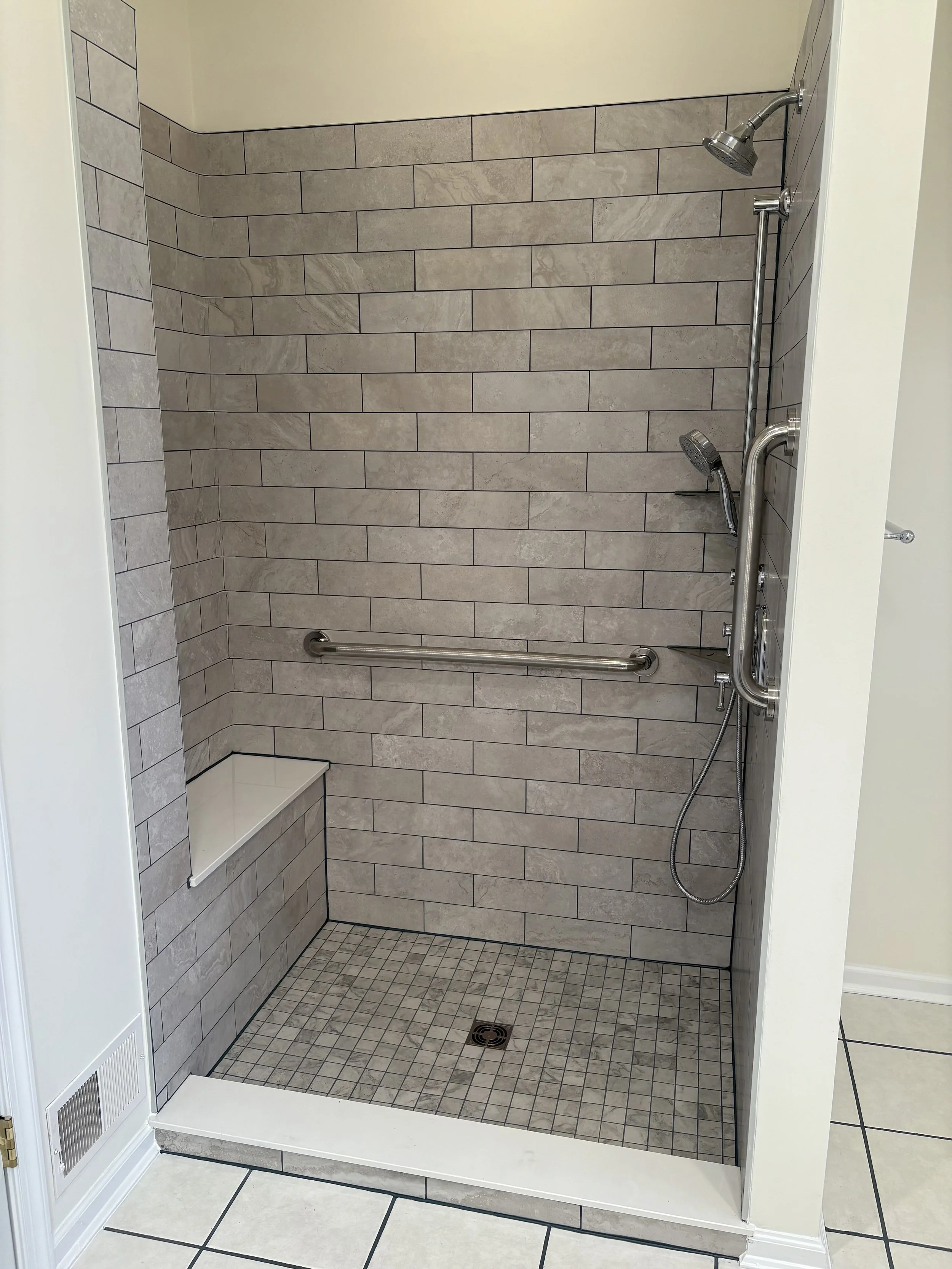 Accessible shower with gray tile walls, built-in seat, and handrails.