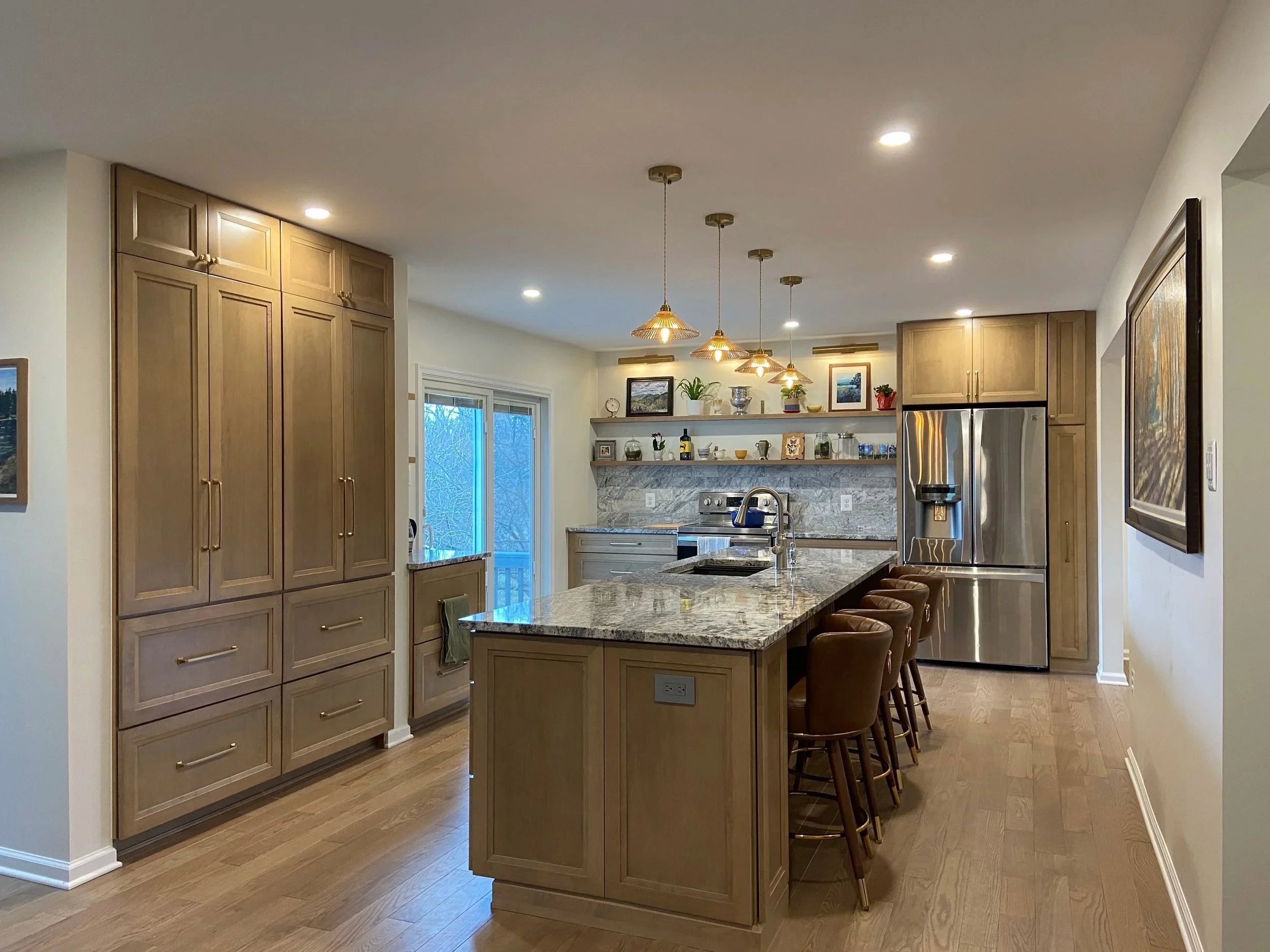 Modern kitchen with wooden cabinets, granite island, stainless steel refrigerator, and open shelving, under pendant lighting and recessed ceiling lights.
